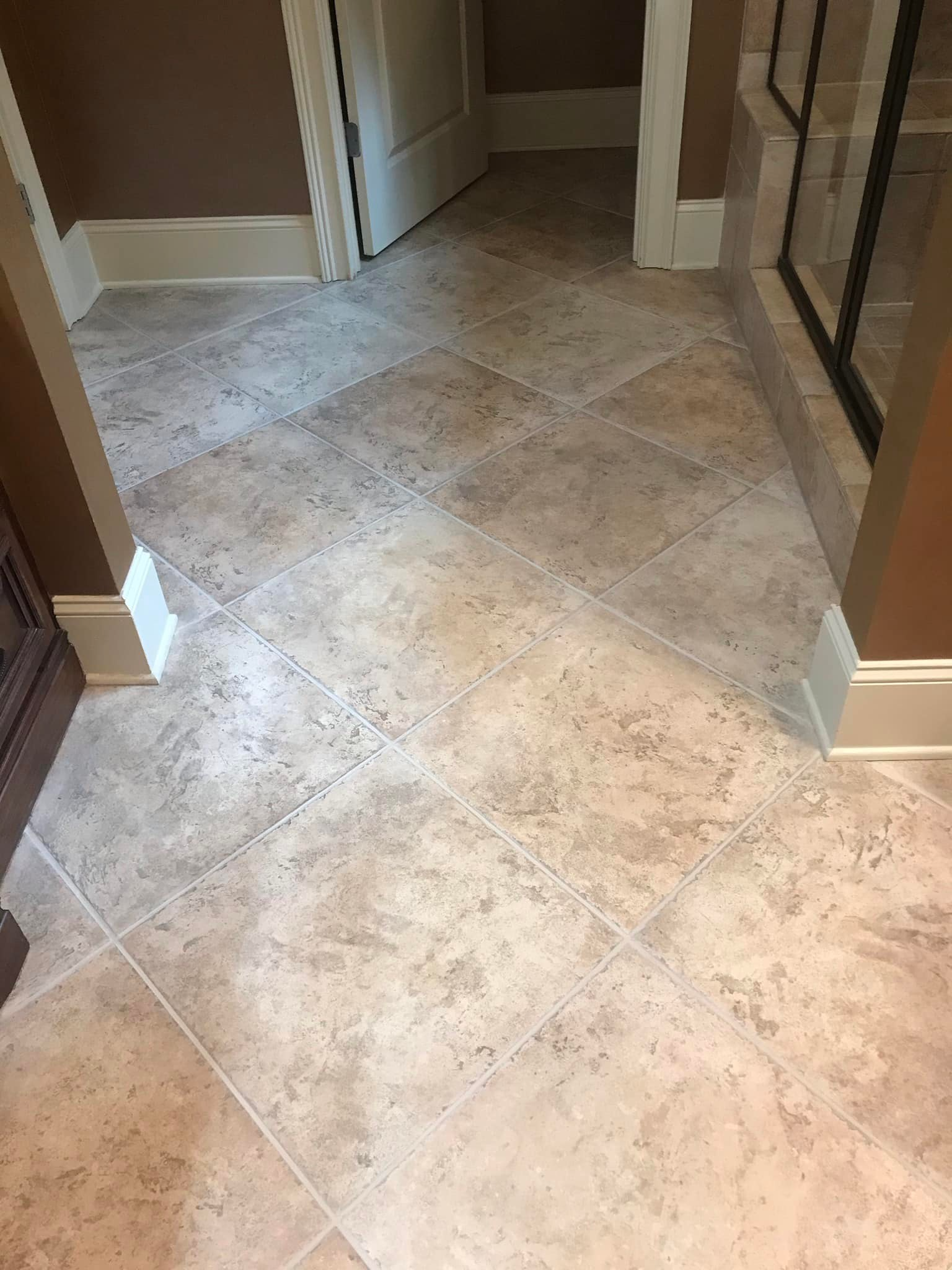 Beige tile floor in a bathroom, with a doorway and shower visible. Brown walls and white trim.