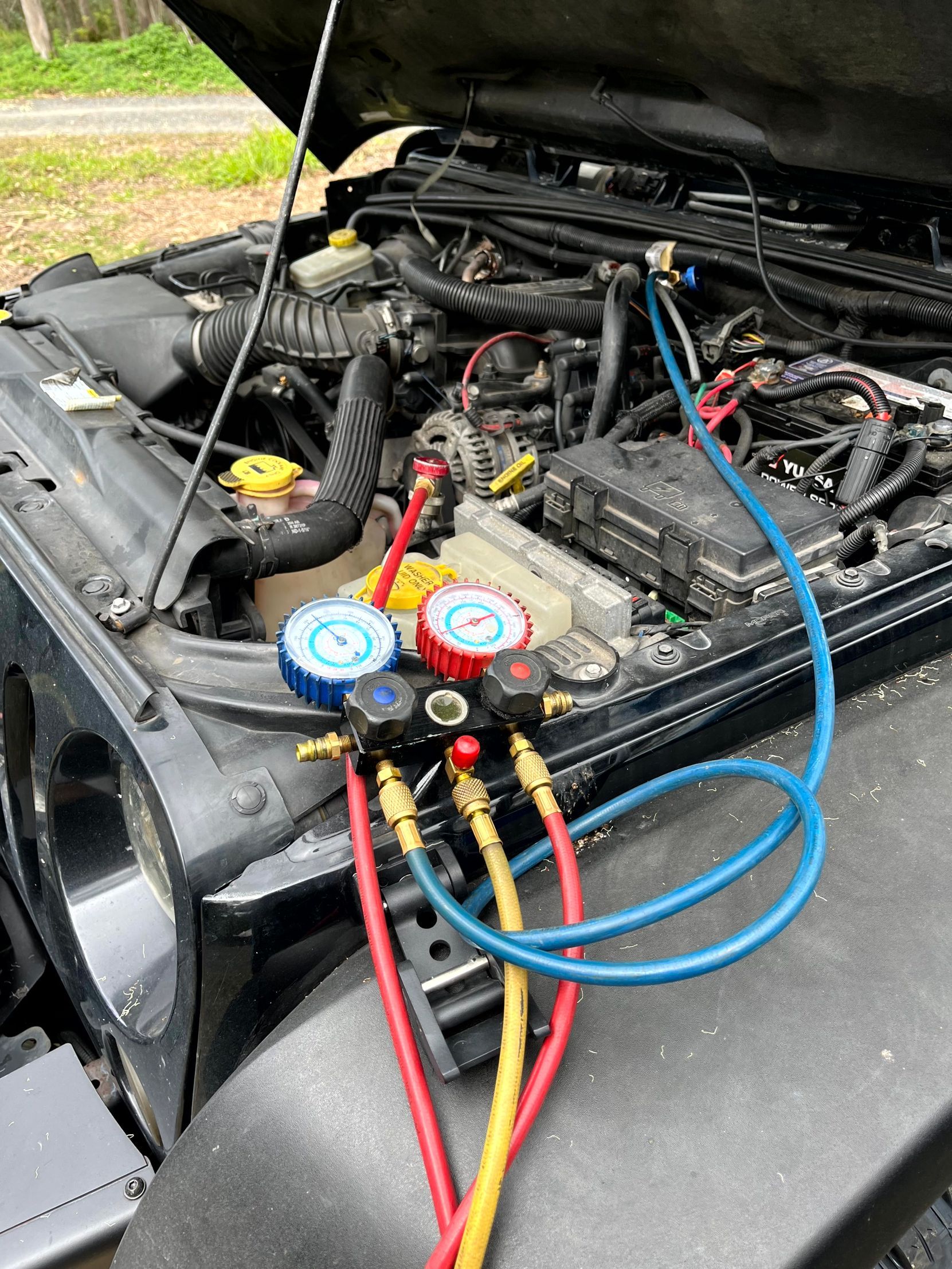 Jeep engine bay with gauges and hoses connected, possibly for AC servicing.
