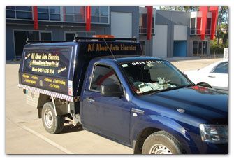 Blue work truck with “All About Auto Electrics” signage parked in a commercial area.