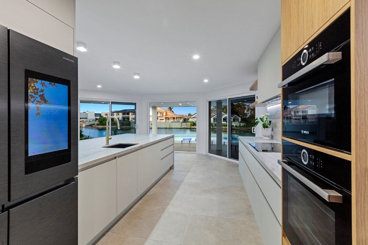 Modern Kitchen With a Large Refrigerator With a Screen, Light-colored Cabinetry, and a View of a Waterway Through Glass Doors — Truline Cabinets In Tuchekoi, QLD
