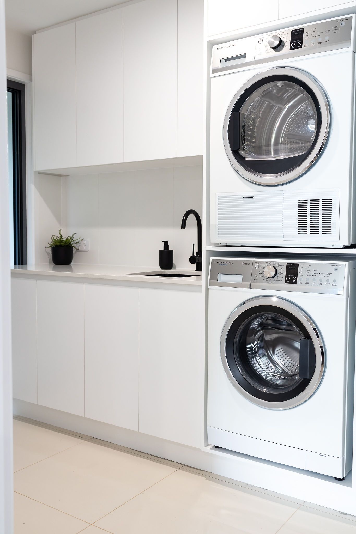 Laundry Room With Stacked White Washer/dryer, White Cabinets, and Black Faucet — Truline Cabinets In Tuchekoi, QLD