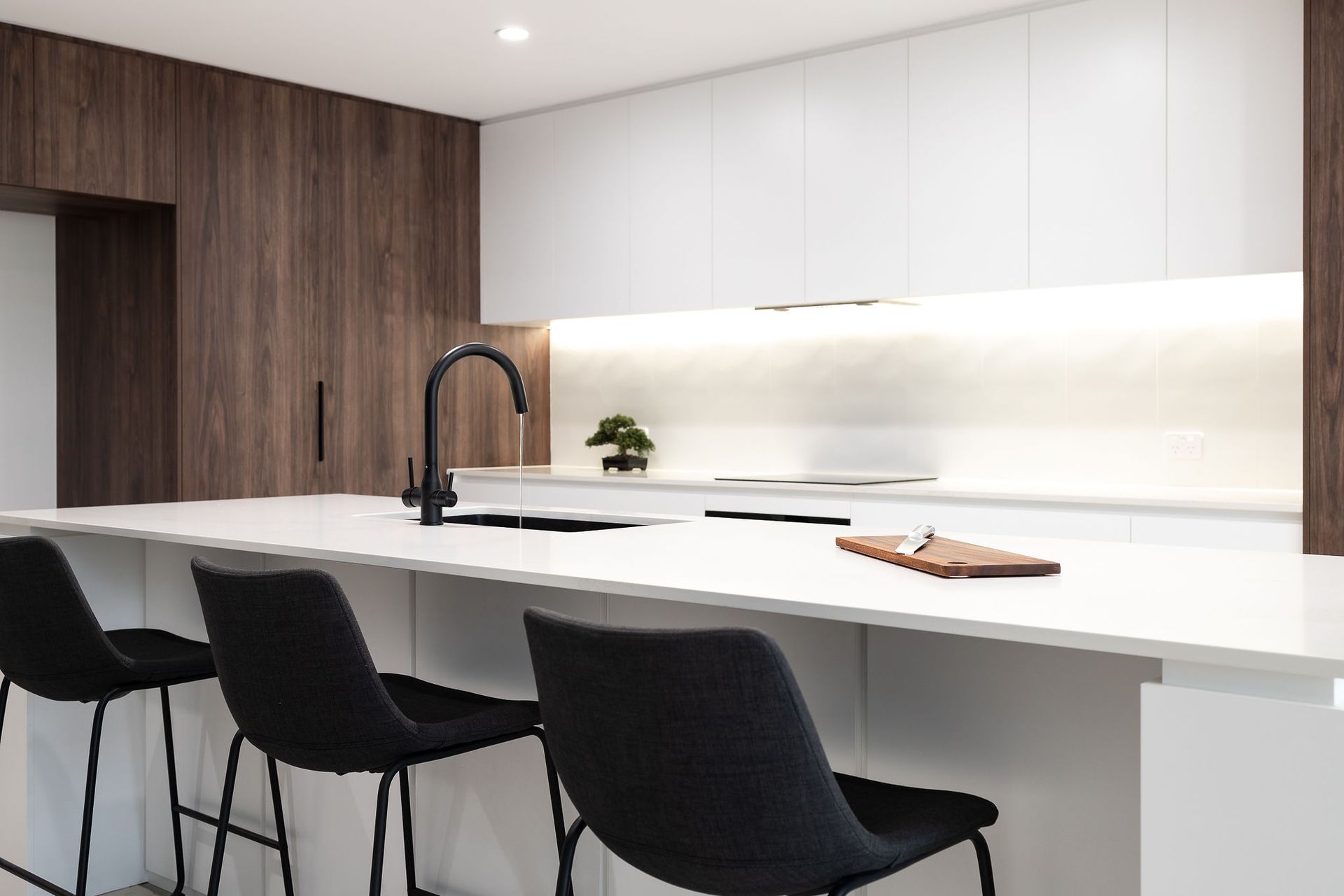 Modern Kitchen With a White Countertop, Dark Wood Paneling, Black Stools, and Faucet — Truline Cabinets In Tuchekoi, QLD