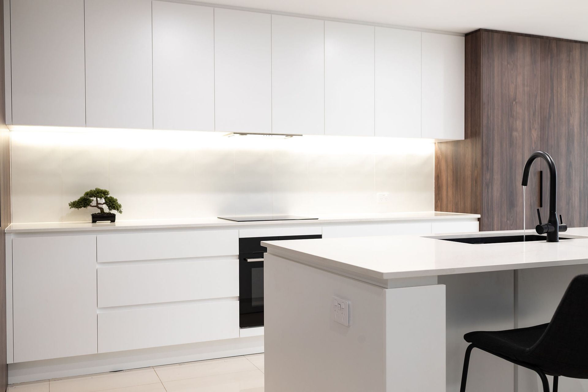 Modern White Kitchen With Island, Dark Faucet, and Wooden Accent Wall — Truline Cabinets In Tuchekoi, QLD