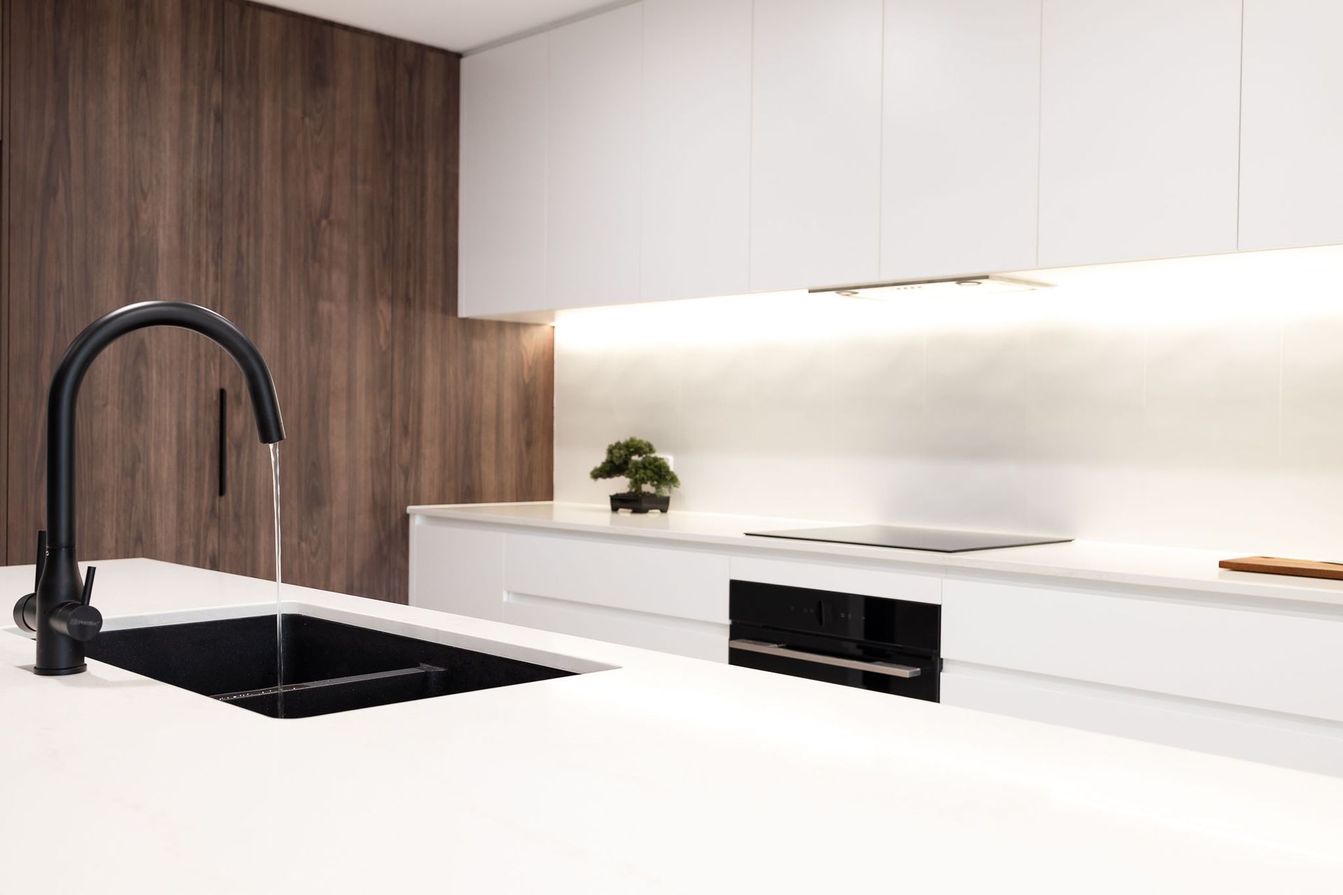 Black Faucet With Running Water in a White Modern Kitchen. Wooden Wall and White Countertops — Truline Cabinets In Tuchekoi, QLD