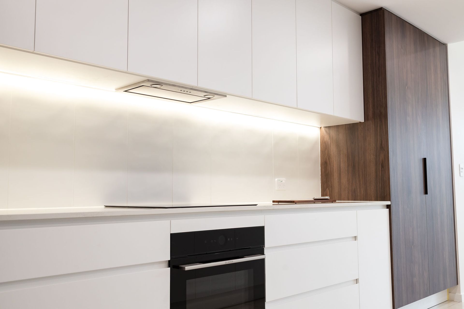 Modern White Kitchen With Dark Oven, Wooden Cabinetry, and Under-cabinet Lighting — Truline Cabinets In Tuchekoi, QLD