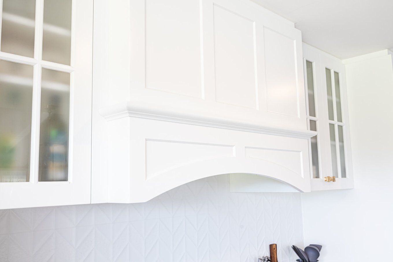 White Kitchen Cabinets With a Decorative Range Hood Above a Tiled Backsplash — Truline Cabinets In Tuchekoi, QLD