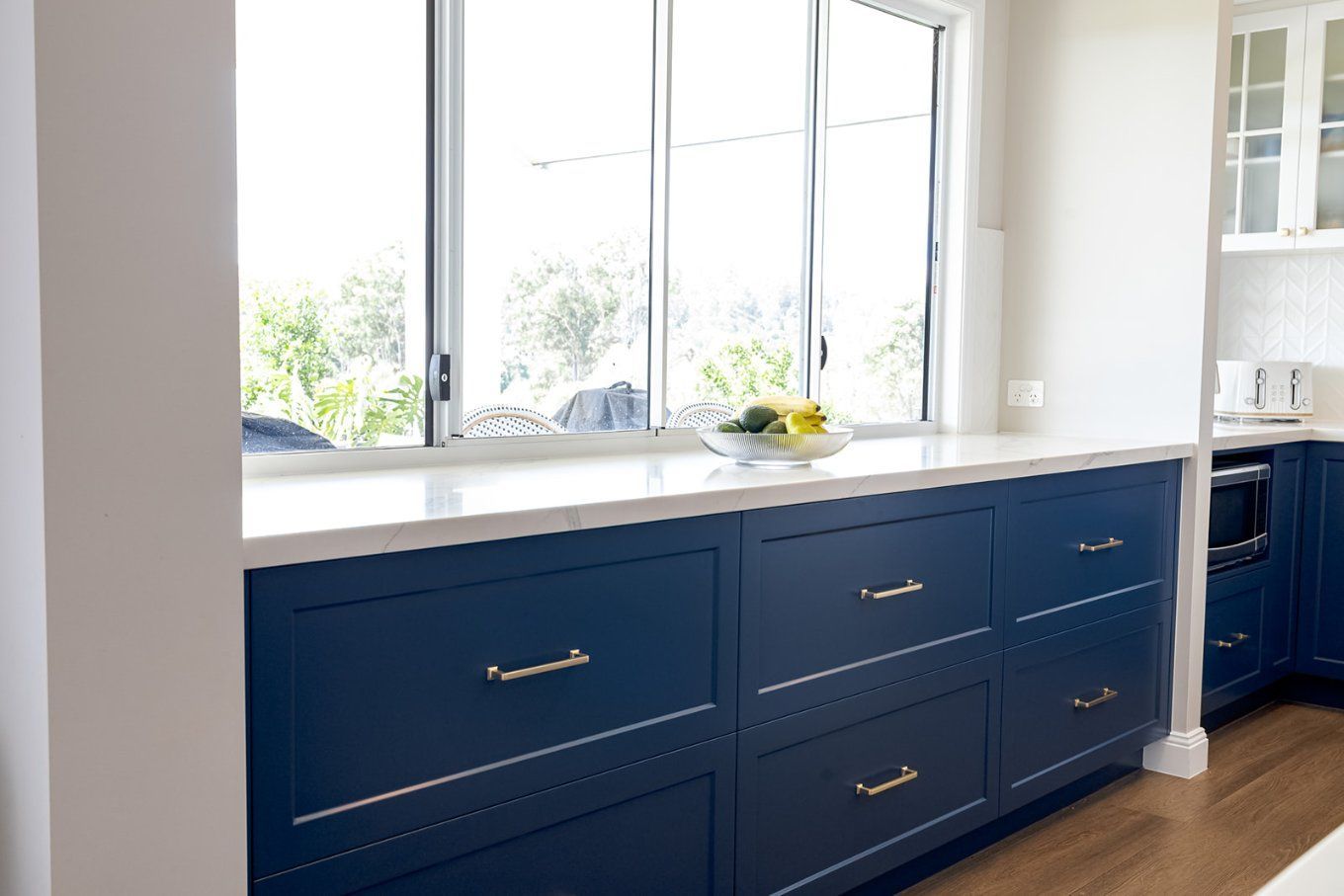 Dark Blue Kitchen Cabinets With White Countertop and a Window Overlooking Greenery — Truline Cabinets In Tuchekoi, QLD