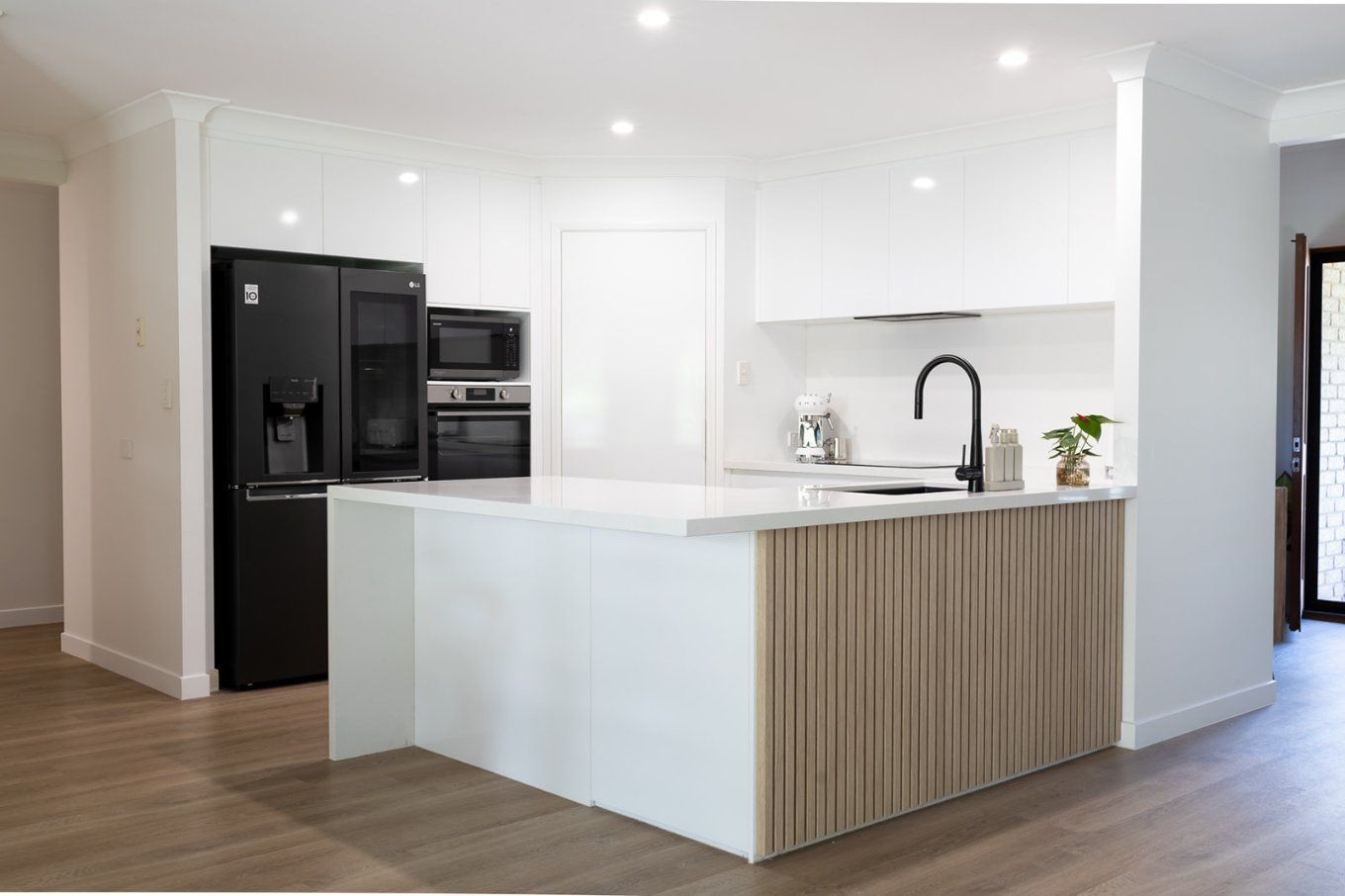 Modern White Kitchen With a Black Refrigerator, Island With Wooden Paneling, and Black Faucet — Truline Cabinets In Tuchekoi, QLD