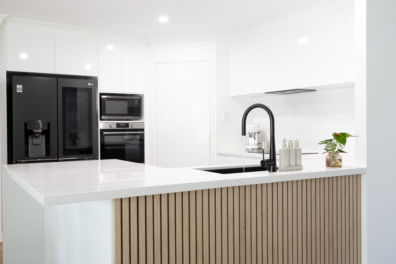 Modern White Kitchen With a Black Refrigerator, Oven, and Sink With a Black Faucet — Truline Cabinets In Tuchekoi, QLD