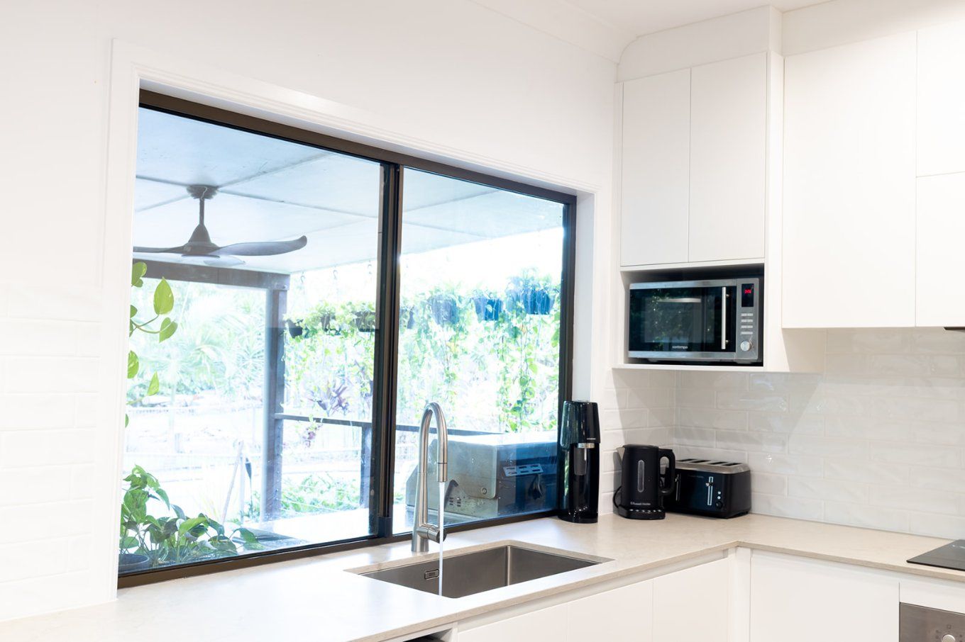 A Bright White Kitchen With a Large Window Overlooking Greenery — Truline Cabinets In Tuchekoi, QLD