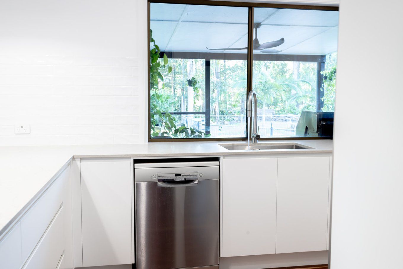 A Modern Kitchen Corner With a Stainless Steel Dishwasher, Sink, and Large Window — Truline Cabinets In Tuchekoi, QLD
