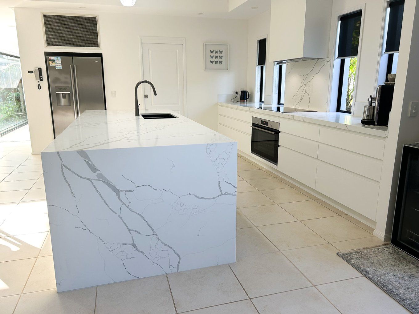 Modern White Kitchen With a Large Island Featuring Marble Countertops and a Black Faucet. White Cabinetry and Tile Flooring Throughout — Truline Cabinets In Tuchekoi, QLD