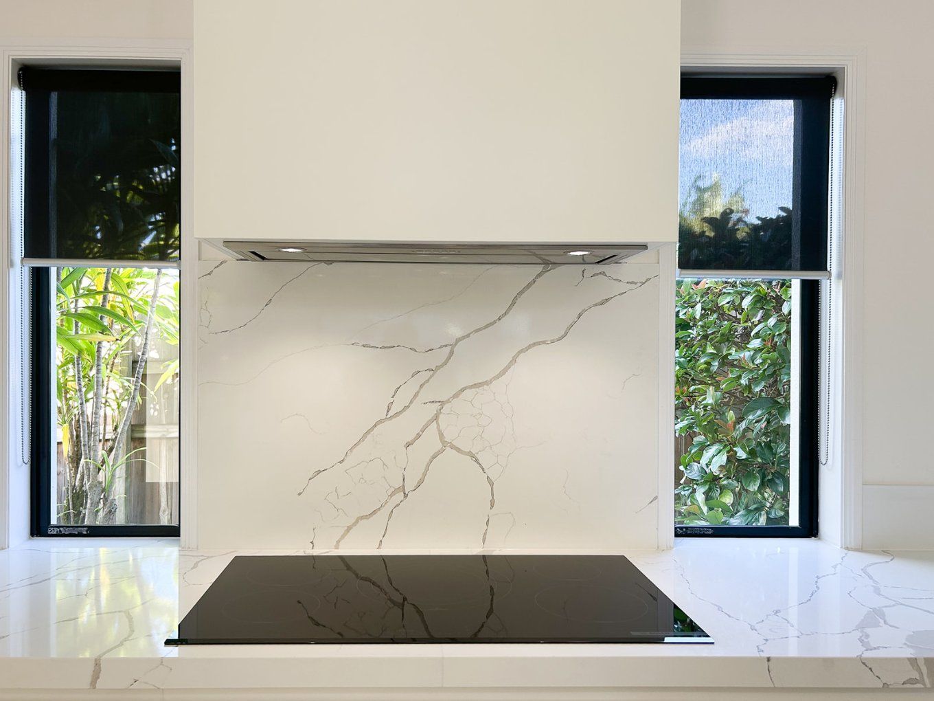 Kitchen With White Marble Backsplash and Countertop, Black Cooktop, Stainless Steel Hood, and Black-framed Windows — Truline Cabinets In Tuchekoi, QLD