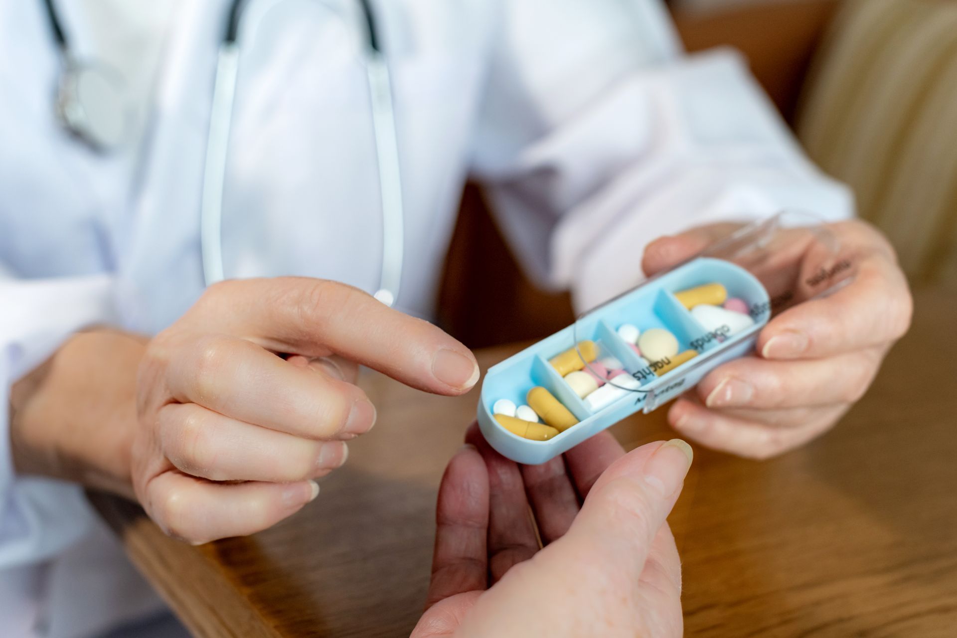 Arzt zeigt auf Pillen in einem Pillenbehälter, den ein Patient hält.