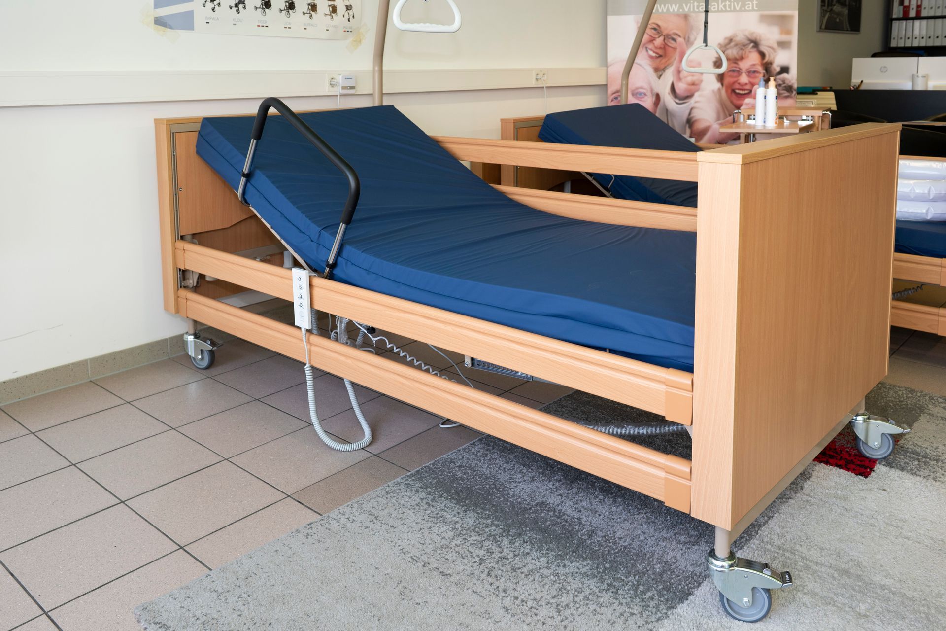 Krankenhausbett, Holzrahmen, blaue Matratze, mit Seitengittern. Auf Rollen in einem Zimmer.