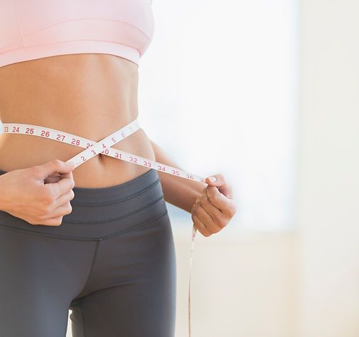 Person measuring waist with a tape measure, wearing black leggings and a pink top