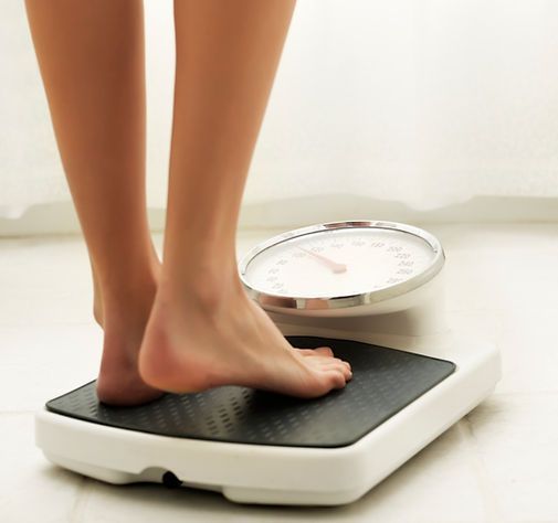 Feet on a white bathroom scale with a black textured platform and analog dial