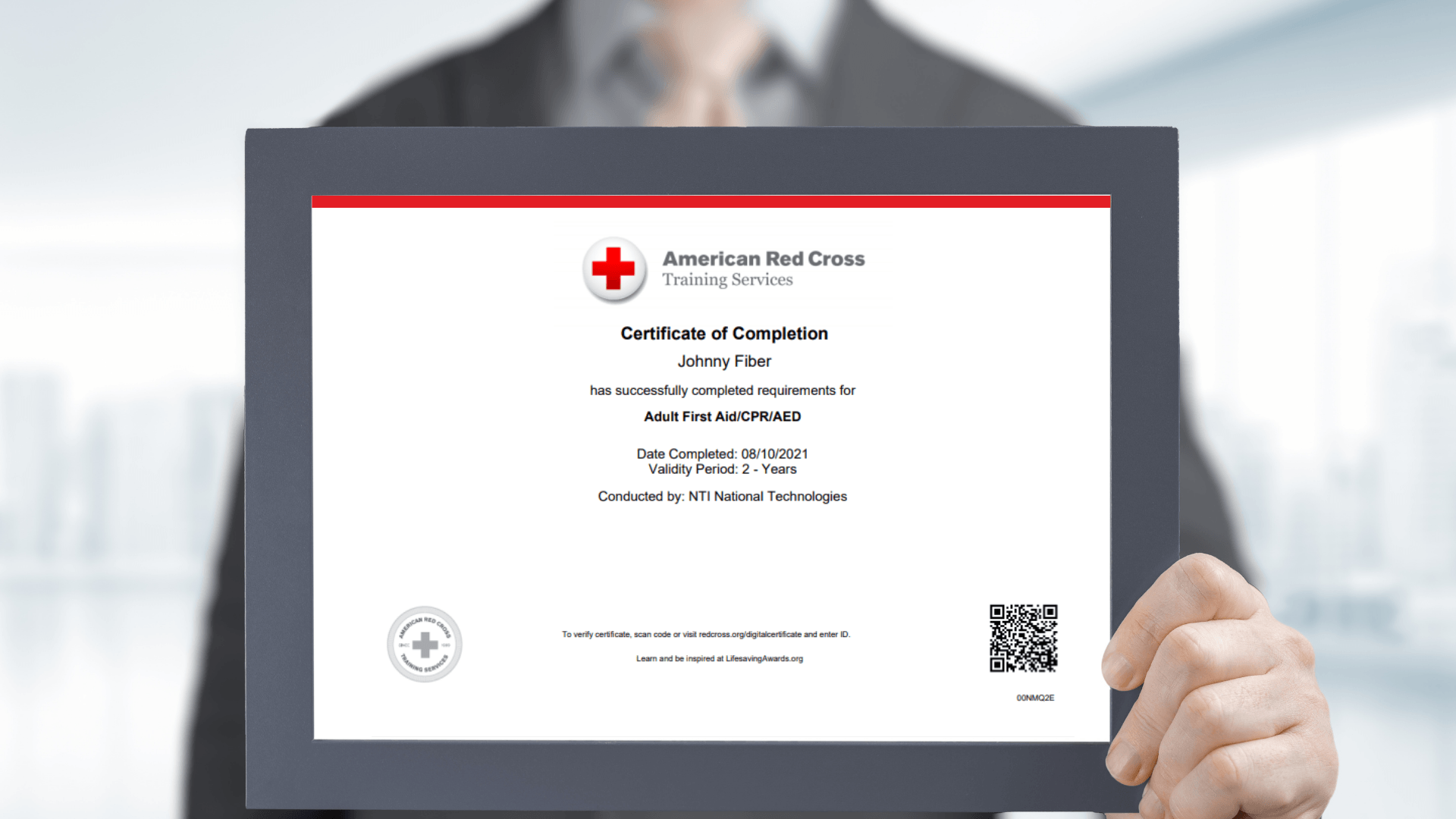 Close up of an American Red Cross certification of training completion being held by a man in the background