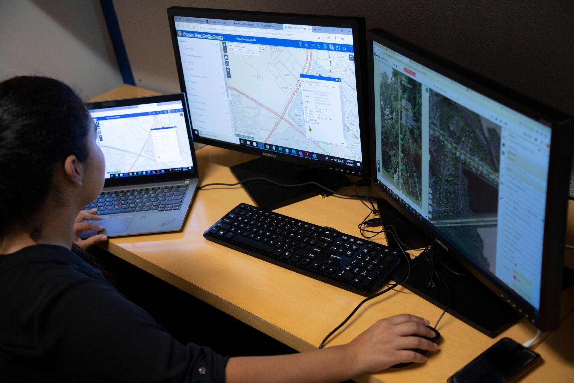 A woman is sitting at a desk with three computer monitors and a laptop.