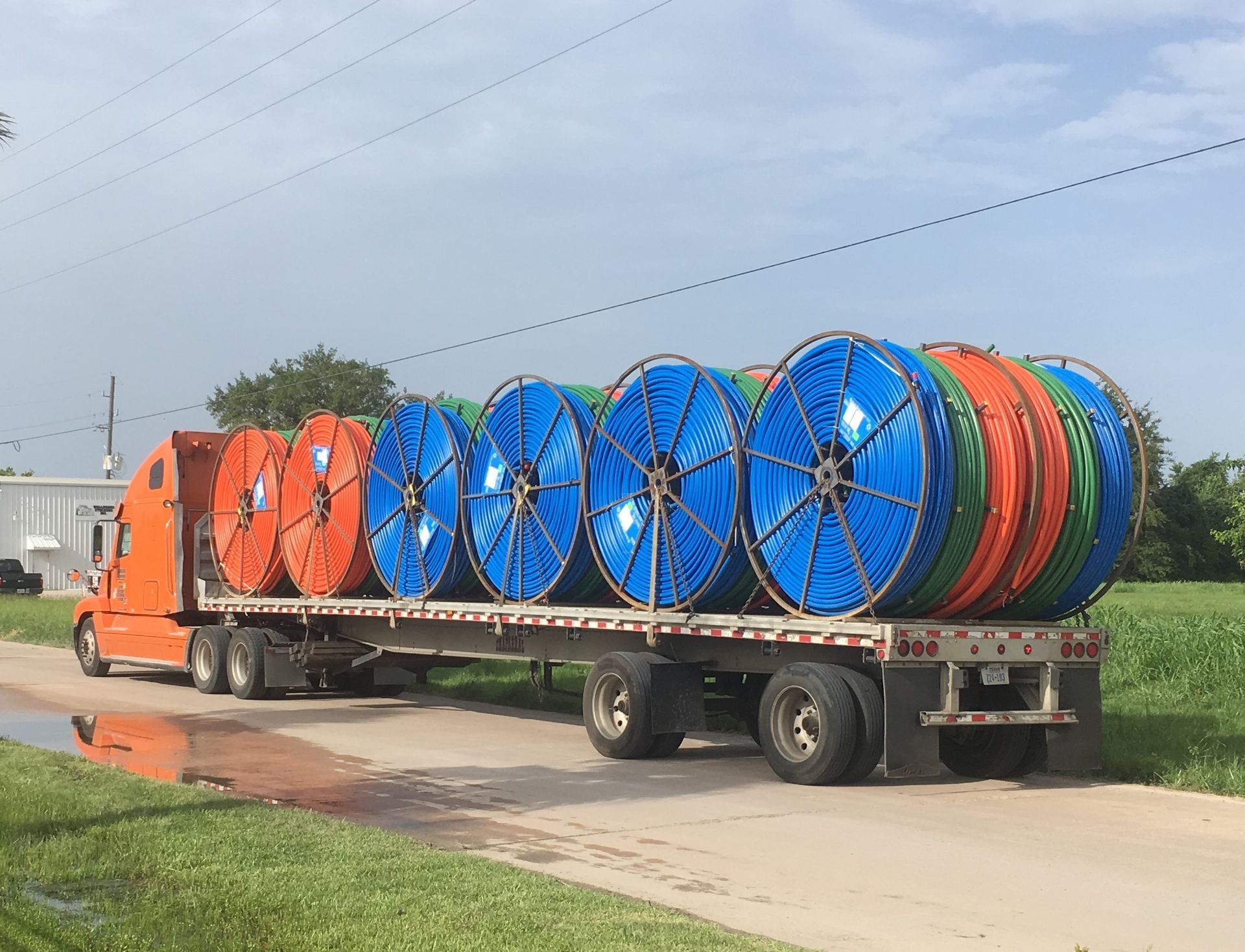 A semi truck is carrying a bunch of spools of hose on a trailer.
