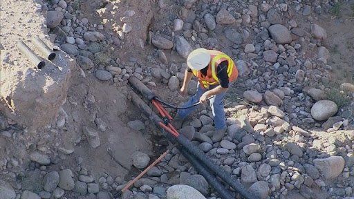 A man is working on a pipe in the dirt.