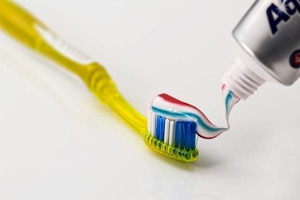 A tube of aquafresh toothpaste is being poured onto a yellow toothbrush