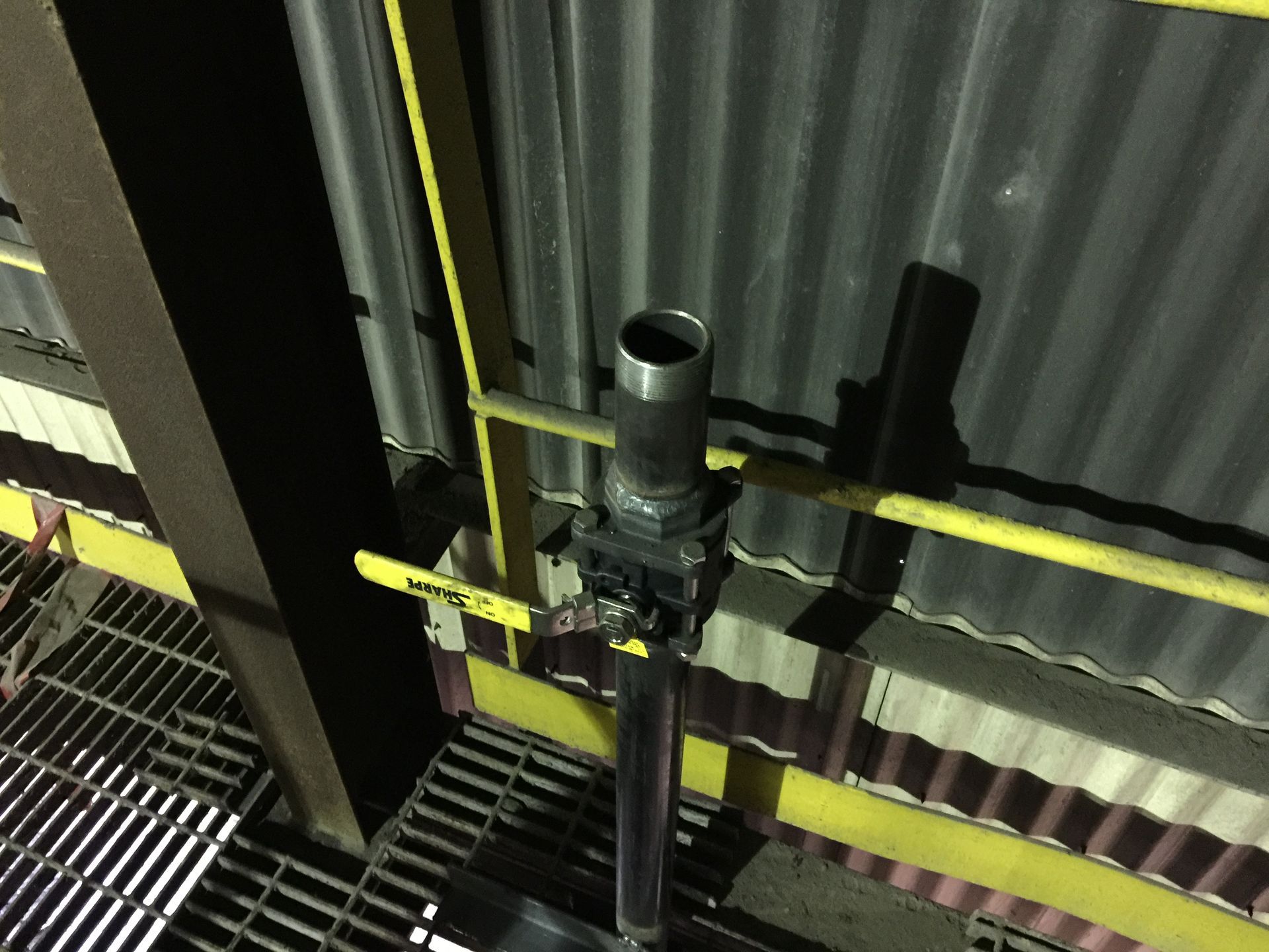 Black pipe with open end, mounted on a yellow-railed platform, against corrugated metal wall.
