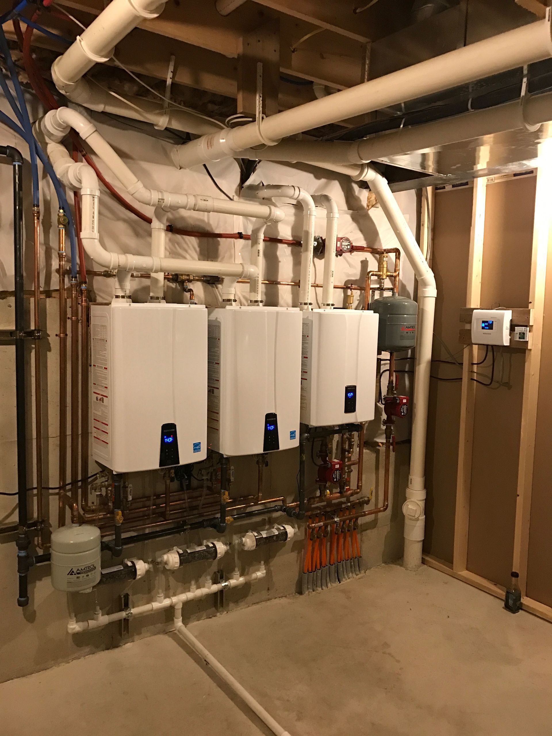 Three white wall-mounted water heaters with complex piping in a utility room.