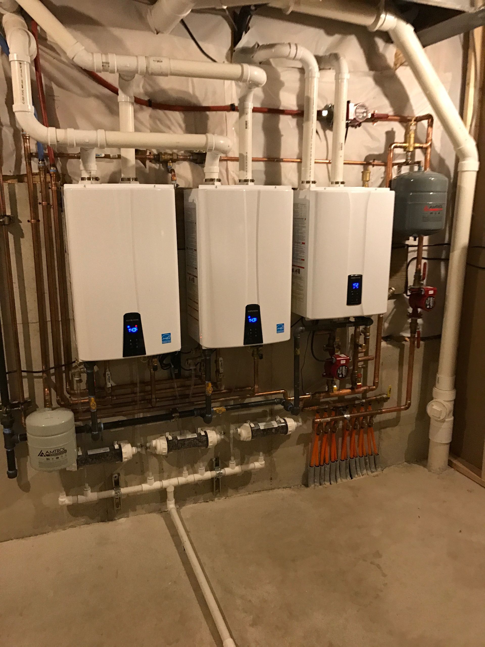 Three white tankless water heaters installed on a concrete wall, with copper and white piping.