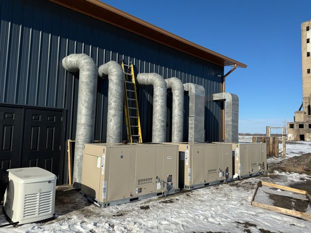 HVAC units with ductwork mounted on the side of a building, ladder leaning against it. Snow on the ground.