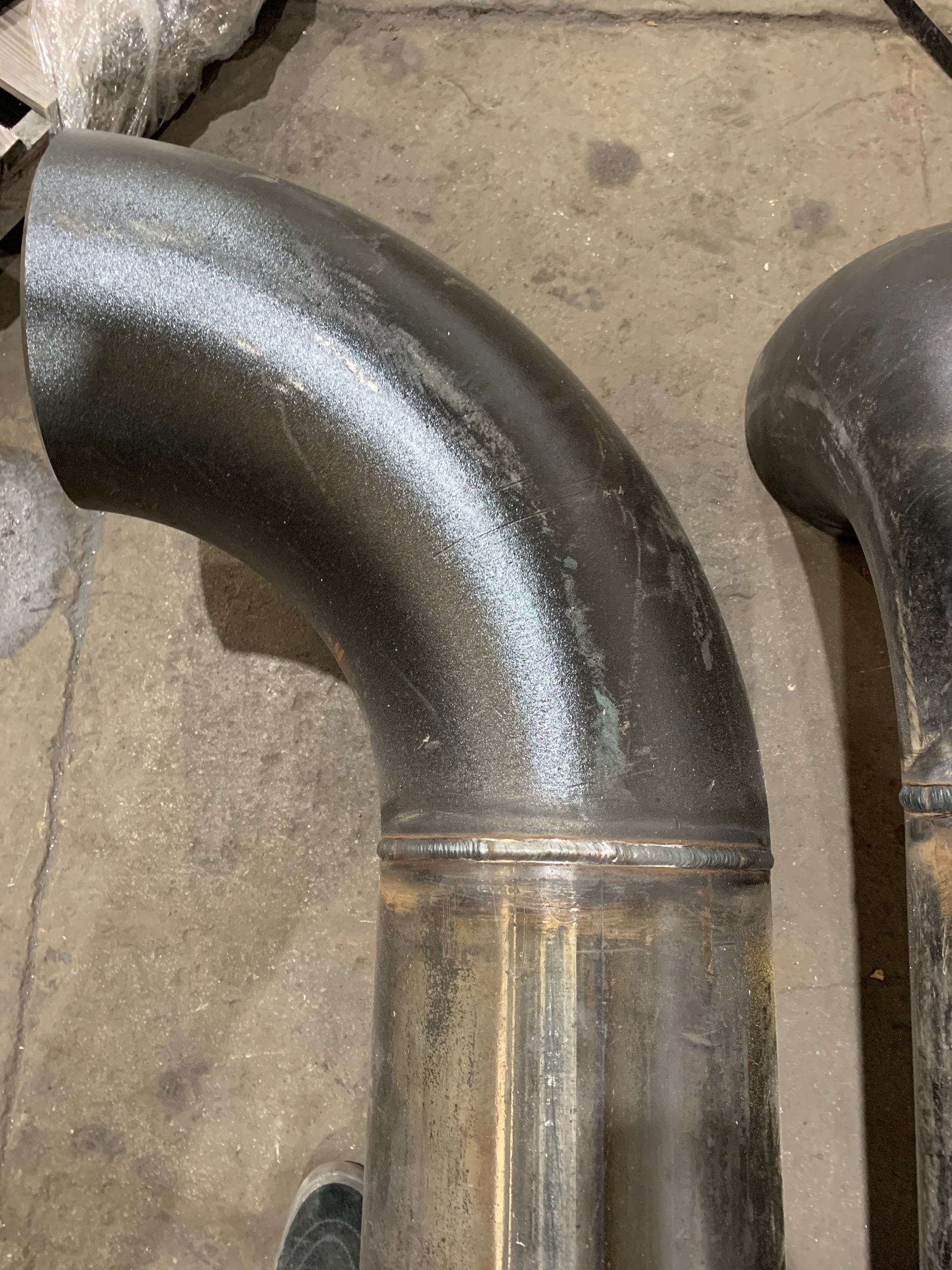Two sections of metal exhaust pipe, one bent, with welds visible.