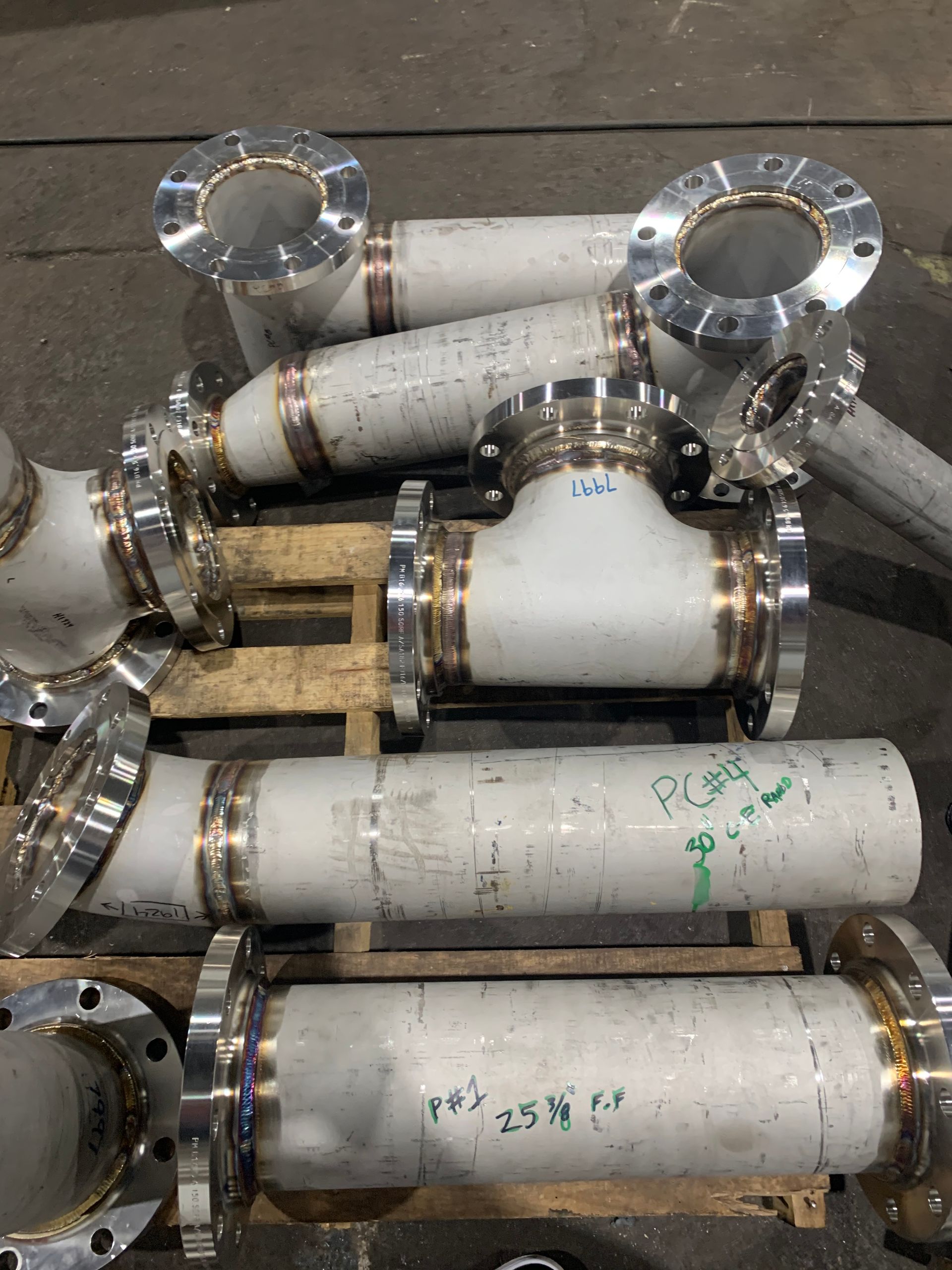 Metal pipes with welded joints and flanges, stacked on a pallet in a workshop.