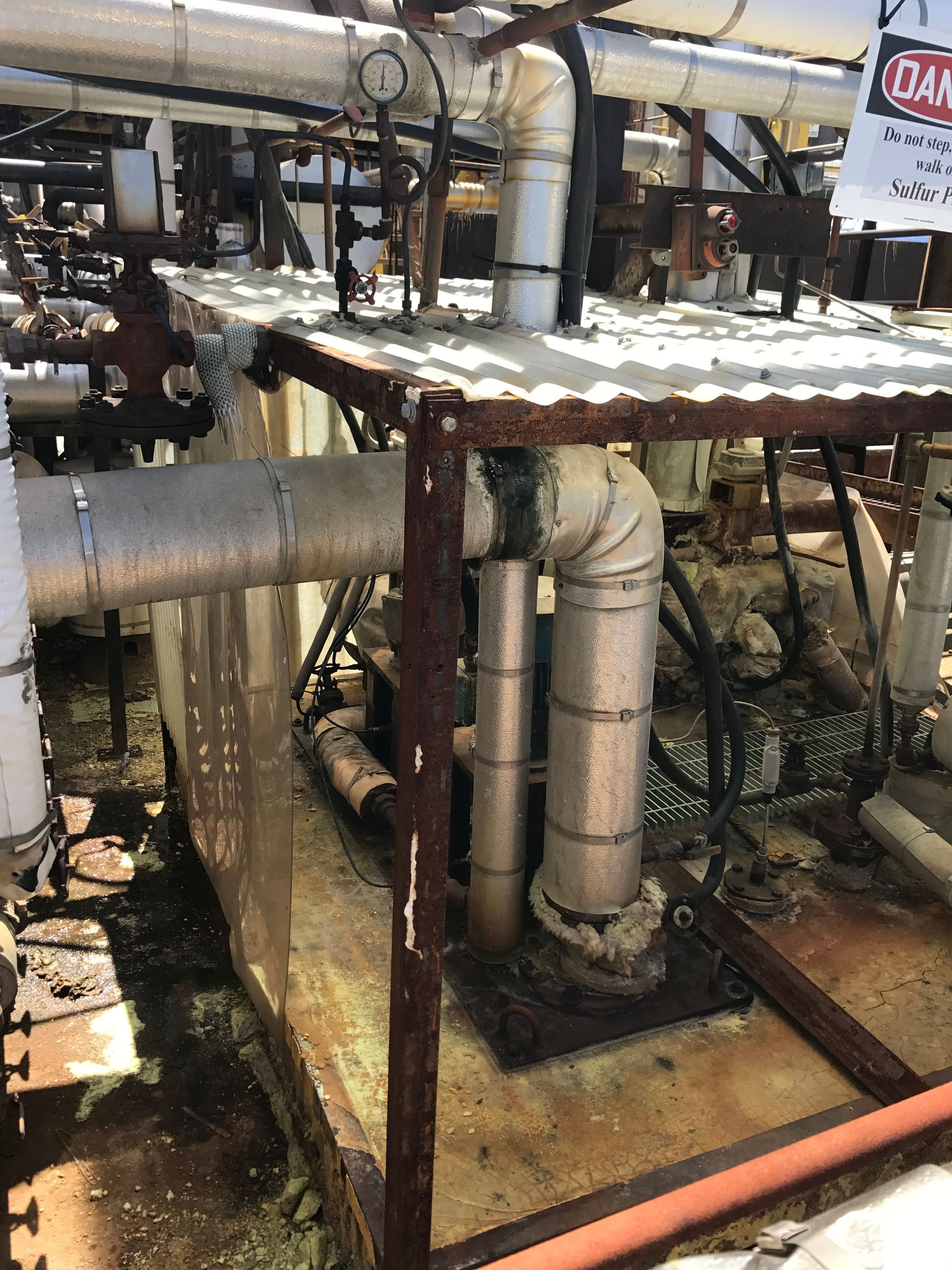 Corroded industrial machinery with pipes, insulation, and warning sign.