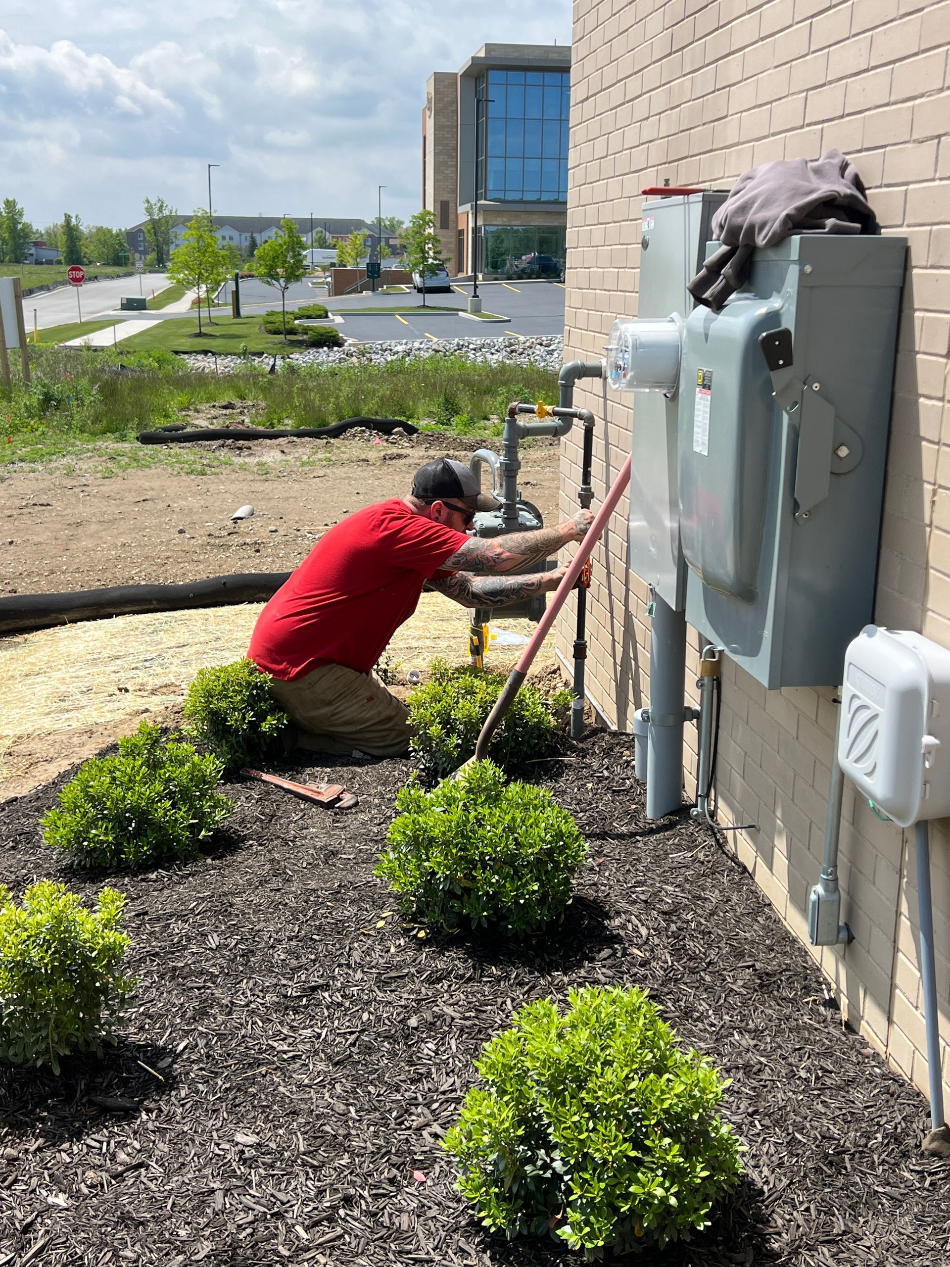 A person in a red shirt works on gas pipes next to a building.