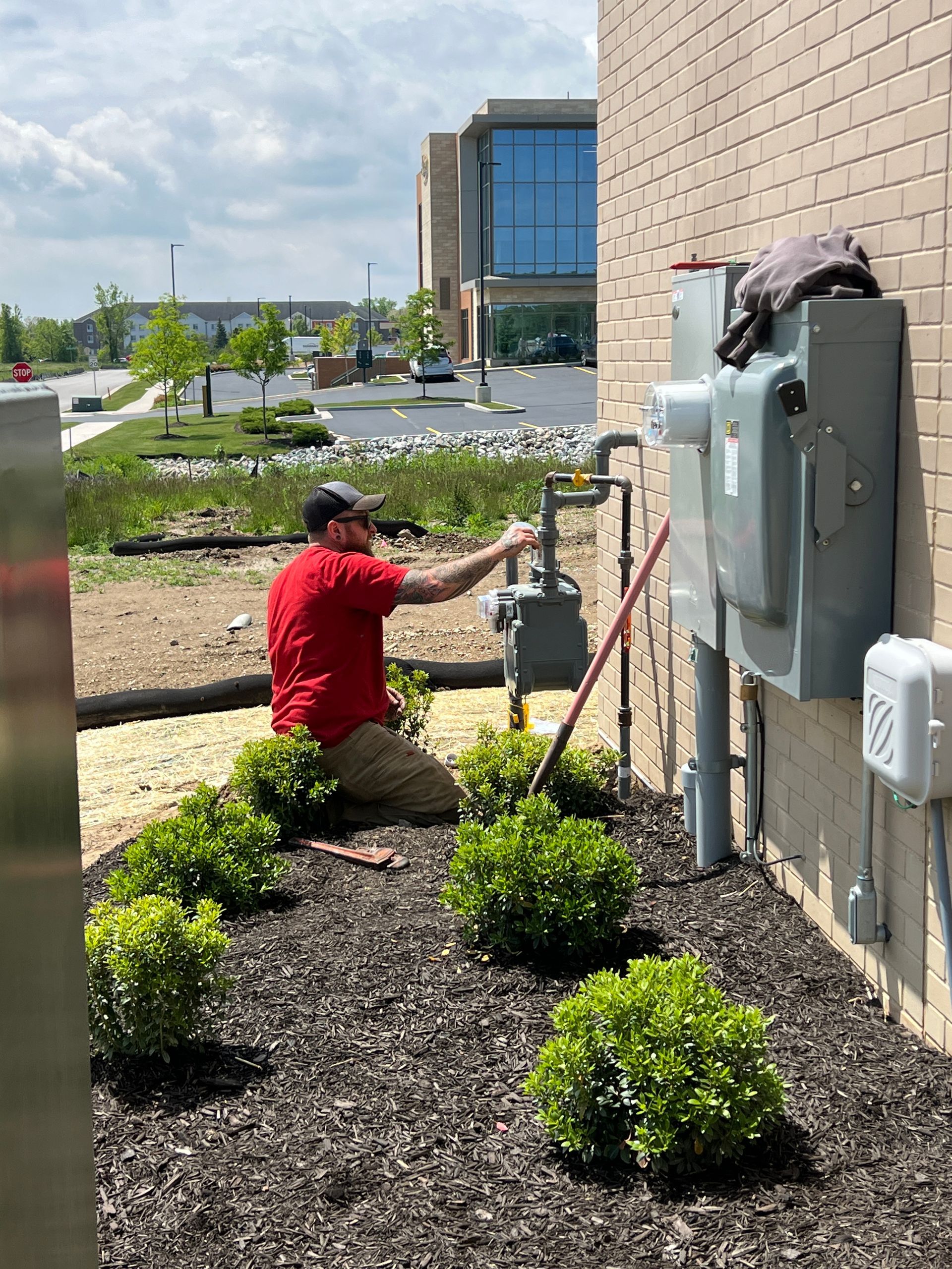 Man in red shirt working on a gas meter on a building, outdoors.