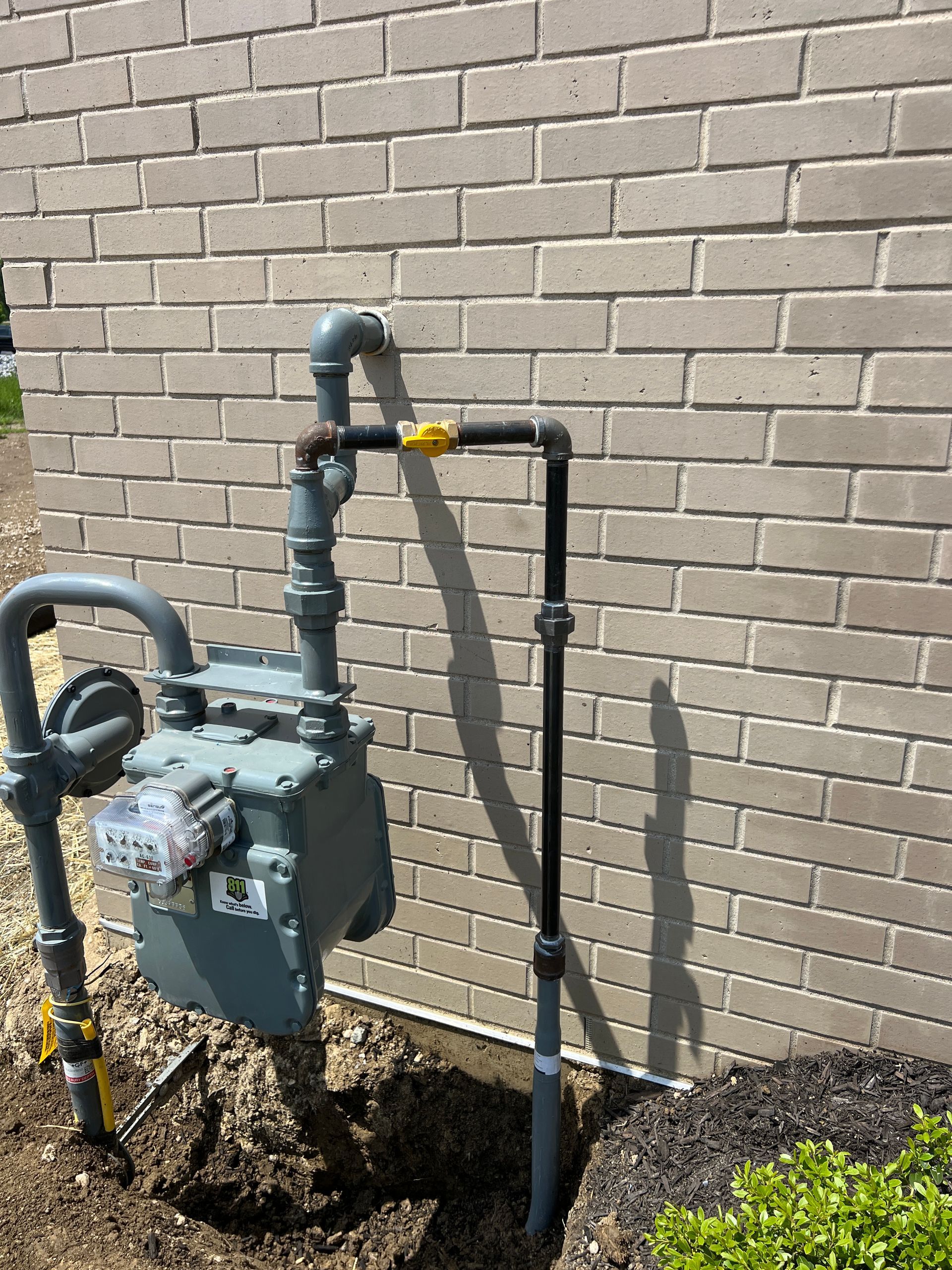 Gas meter and black pipe attached to a brick wall. Gray and yellow pipes connect to the meter.