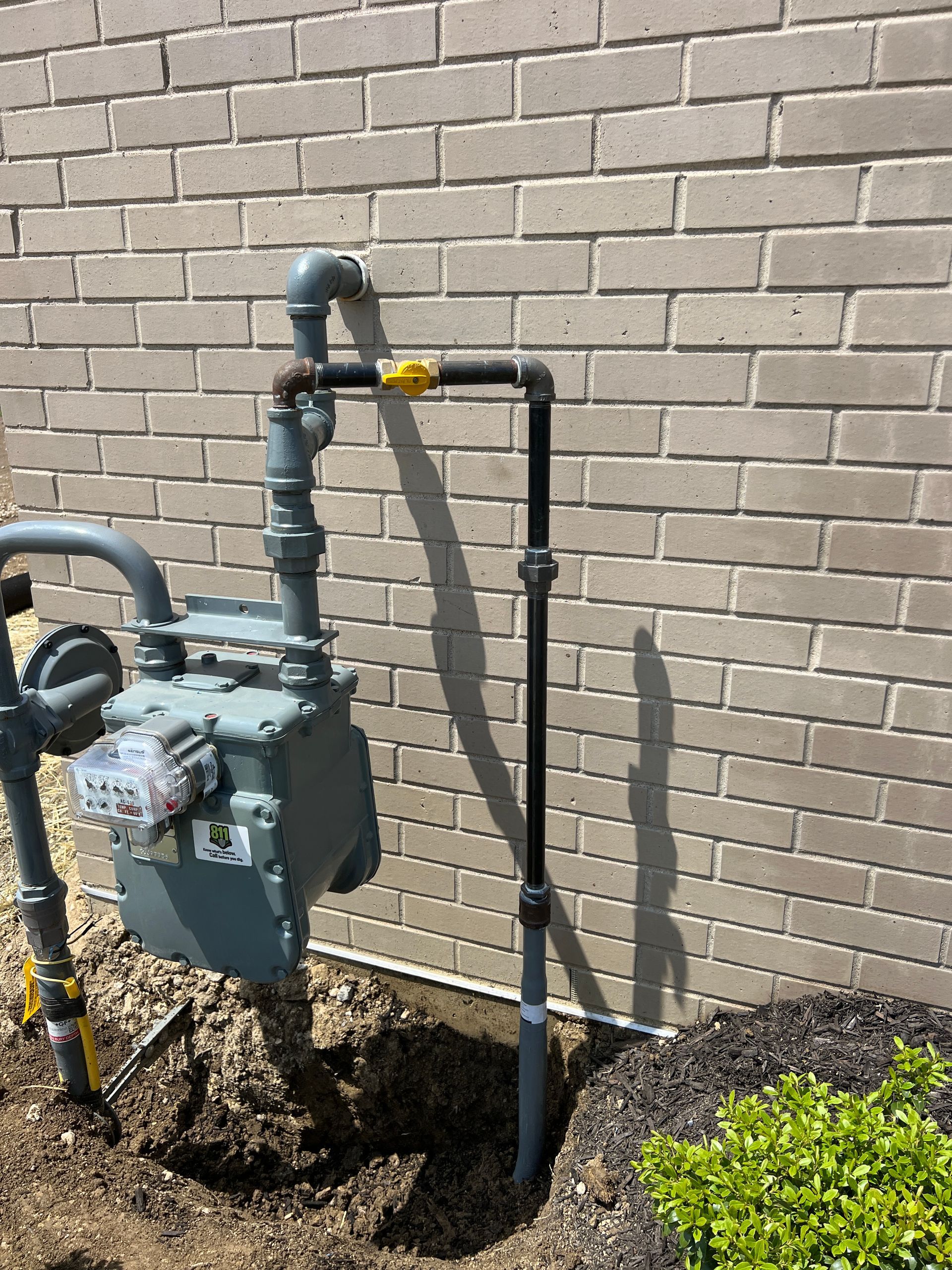 Gas meter and pipes attached to a brick wall. Black and grey pipes with a yellow valve.