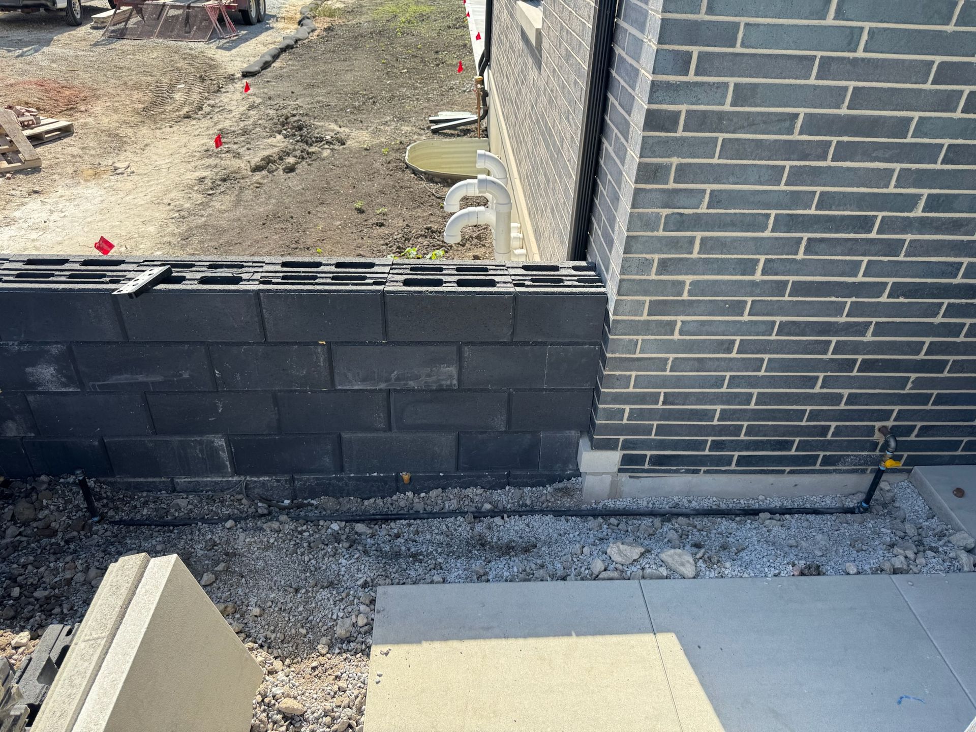 Construction site: black shingle wall next to a brick wall. Gray gravel and cement blocks visible.