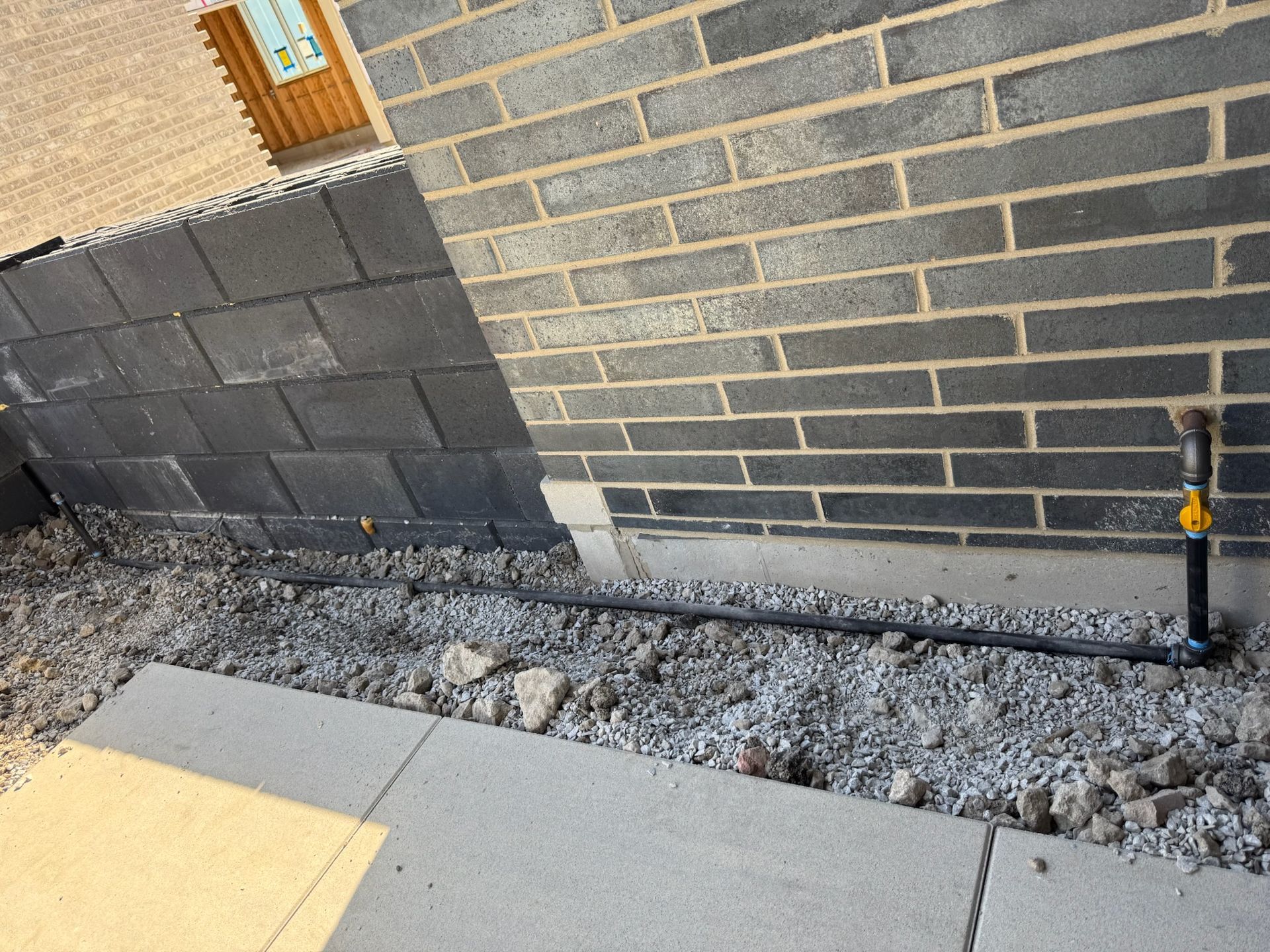 Exterior brick wall under construction with gravel and concrete patio.