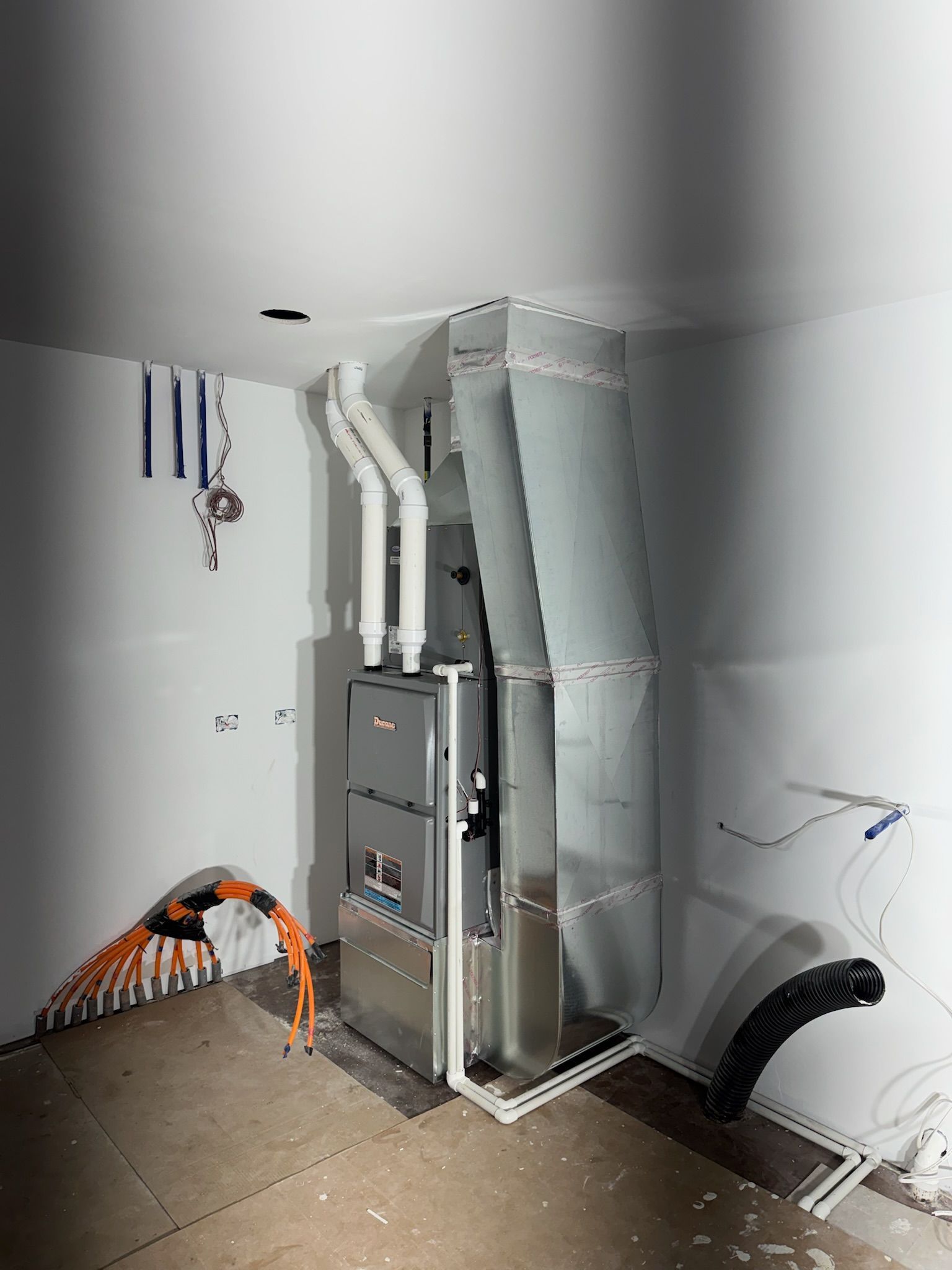 Furnace unit installed in a white-walled room with ductwork, piping, and wiring.