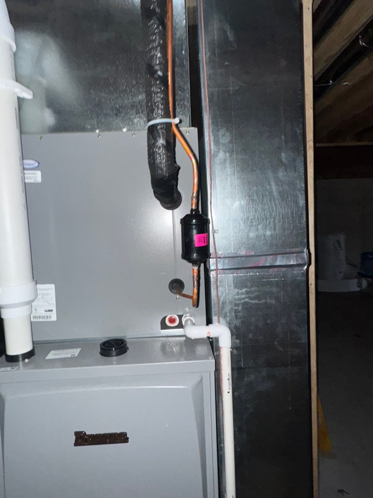 Furnace with copper pipes, filter, and venting in a metal enclosure within a basement setting.