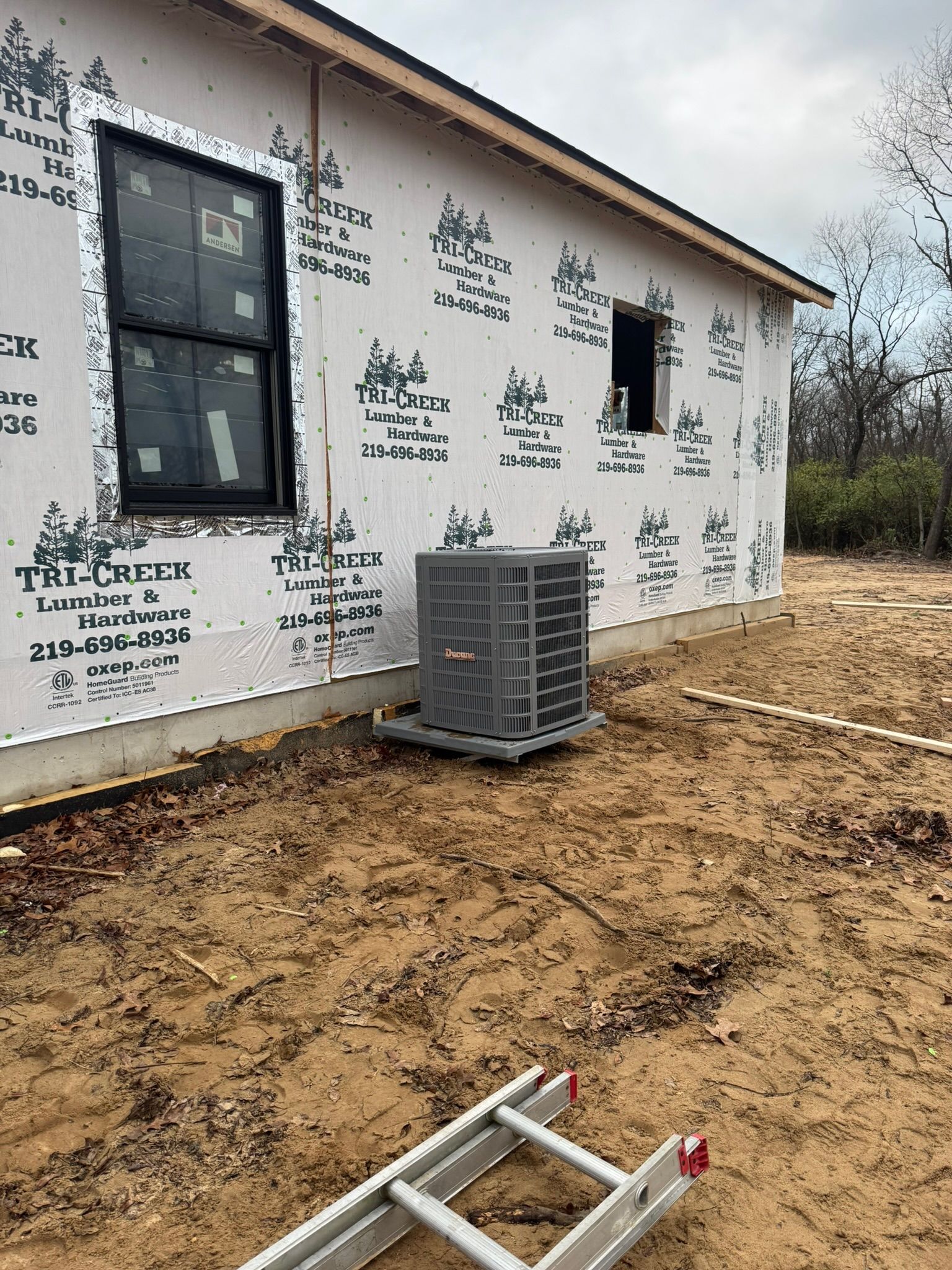 Exterior of a new house under construction; air conditioning unit outside, windows, and ladder on the ground.