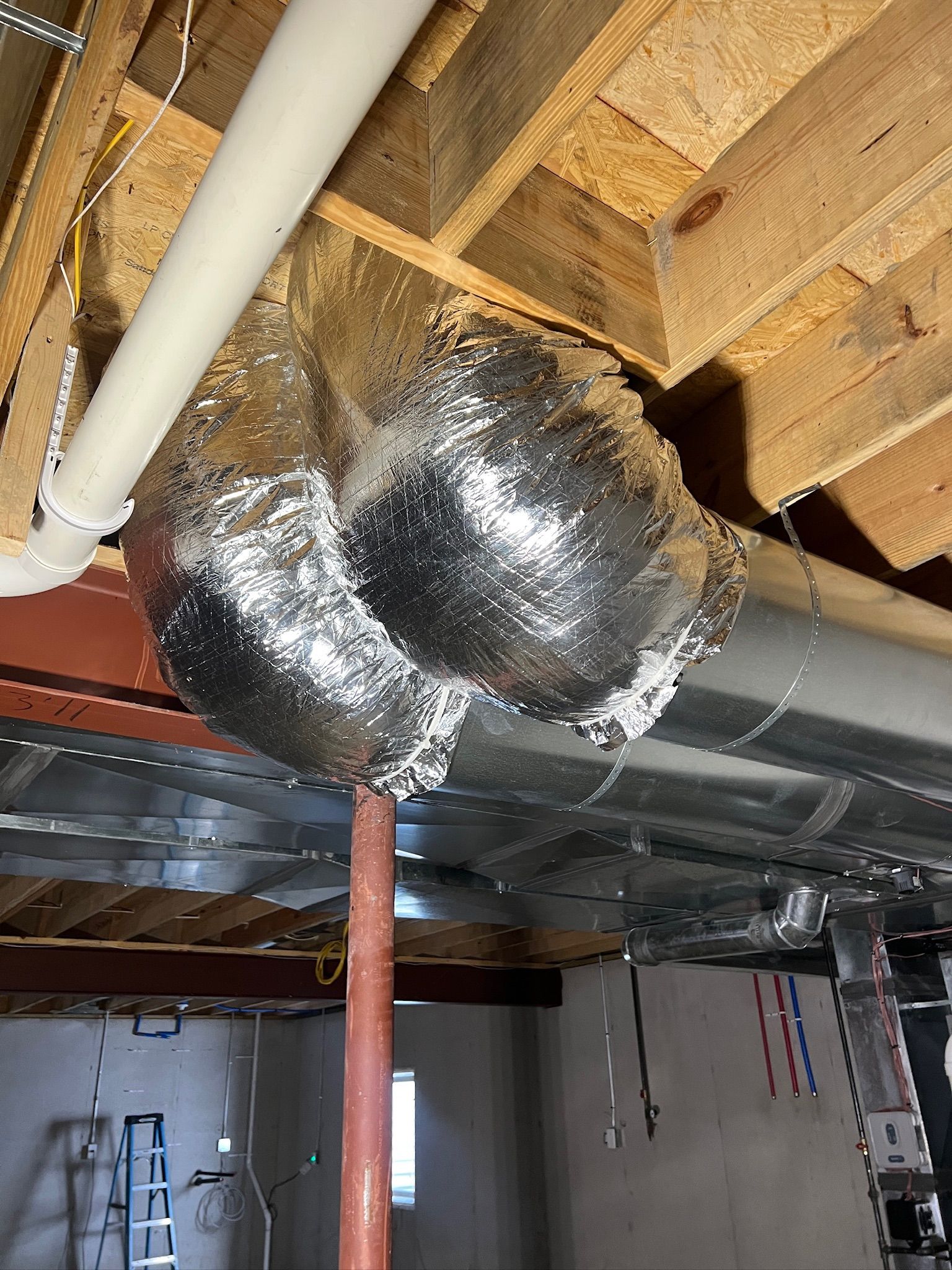 Insulation wrapped around ductwork in a basement ceiling, near a plumbing pipe.
