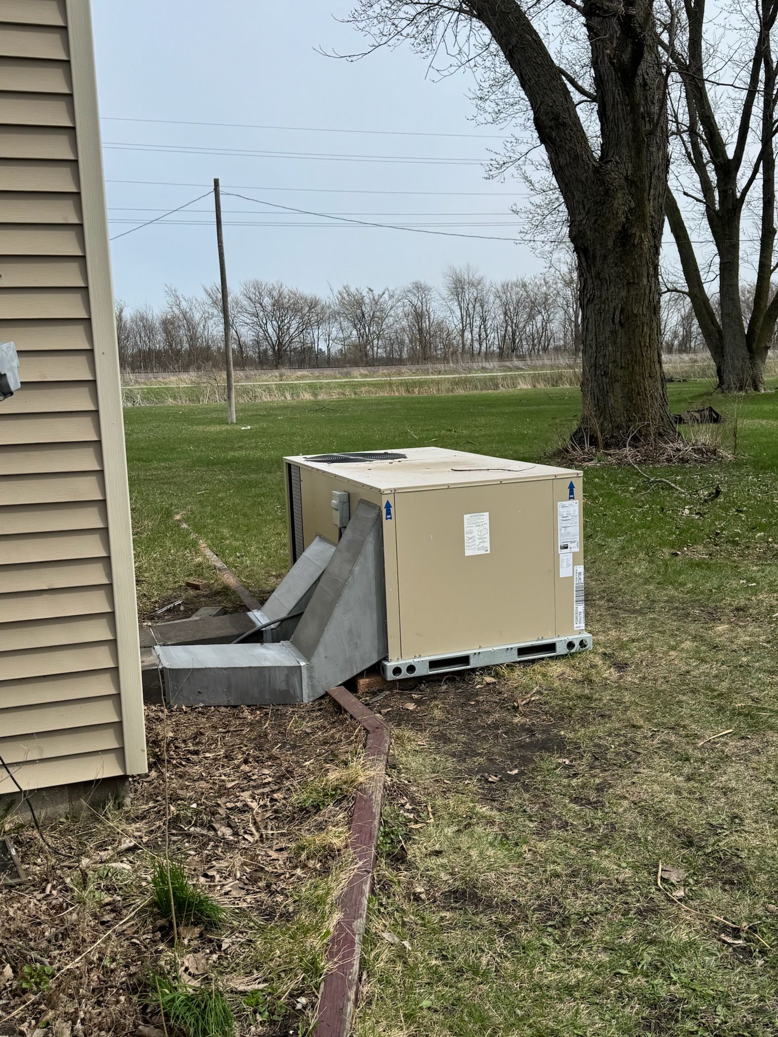 HVAC unit in a box next to a house, on a concrete pad, on grass. Trees and sky in the background.