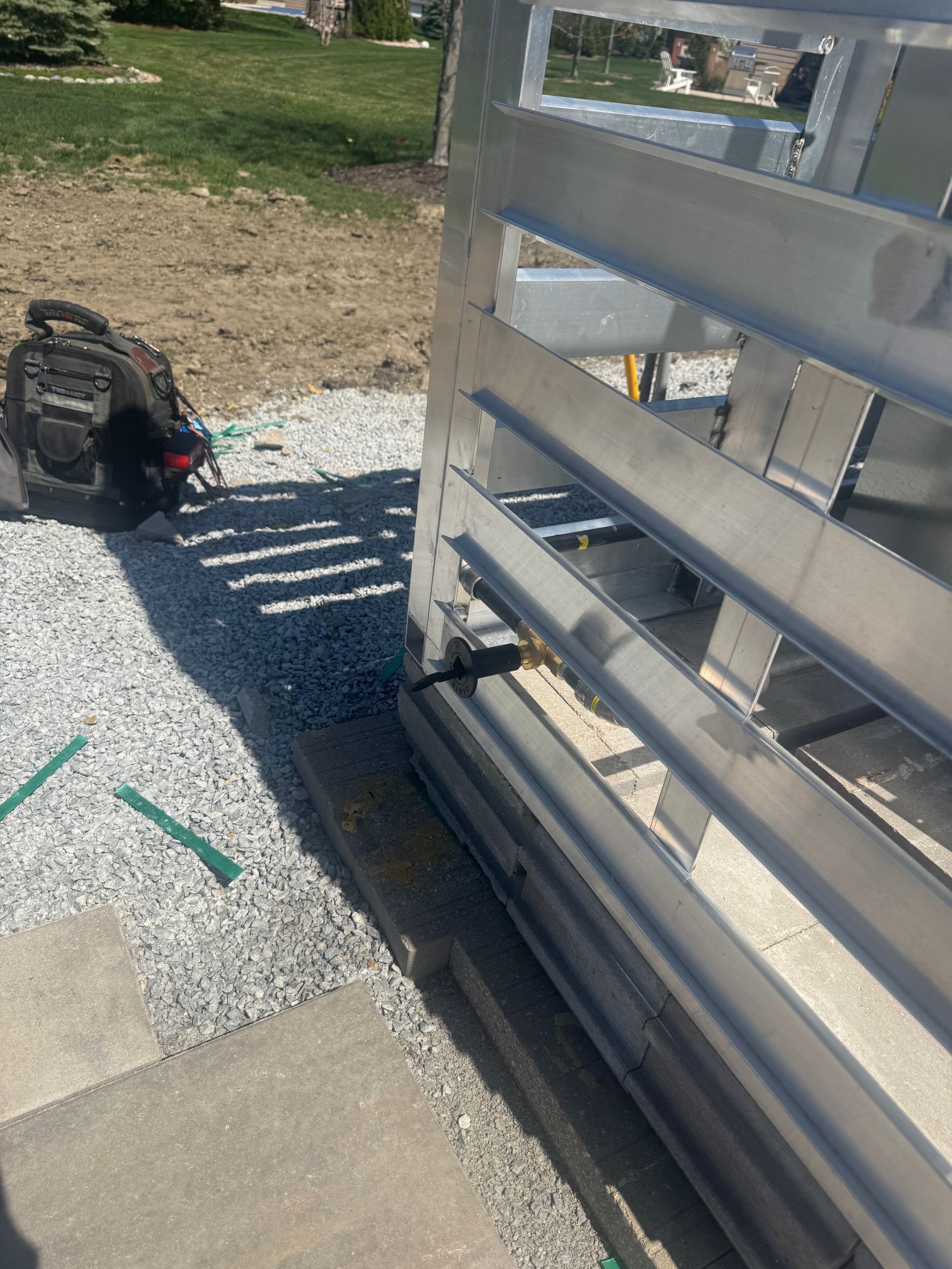 Metal gate, partially open, on gravel path next to brick and grass. A toolbox sits nearby.