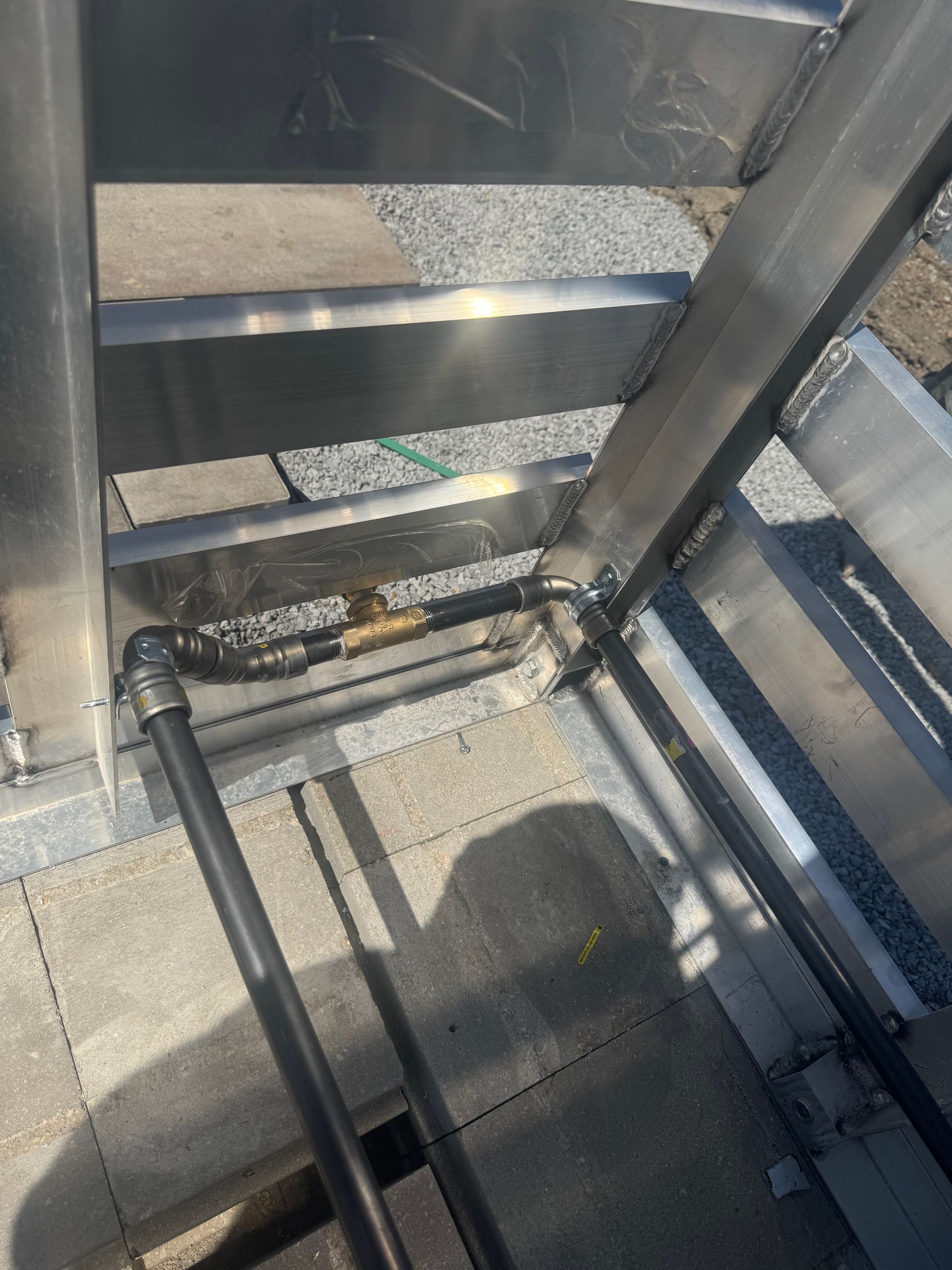 Metal staircase with black pipes and a gold-colored valve. Grey concrete and gravel are visible.