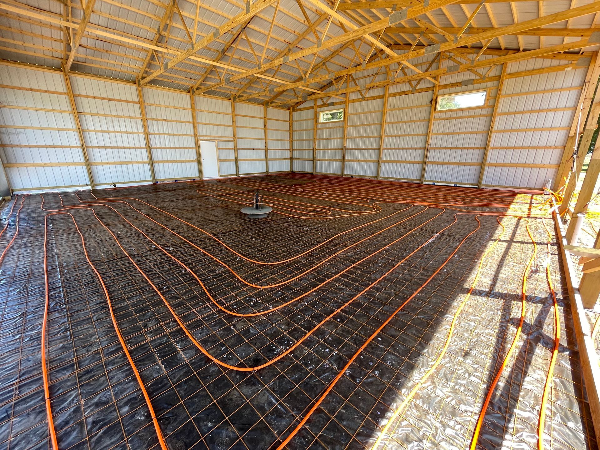 Interior of a large unfinished building with orange tubing laid on a black underlayment across the floor.