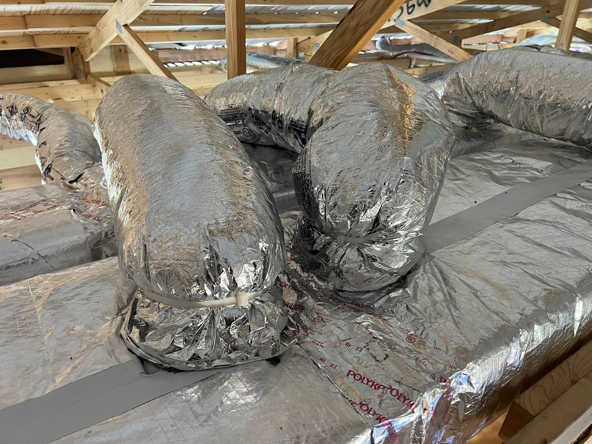 Silver insulated ductwork in an attic, running along a reflective surface.