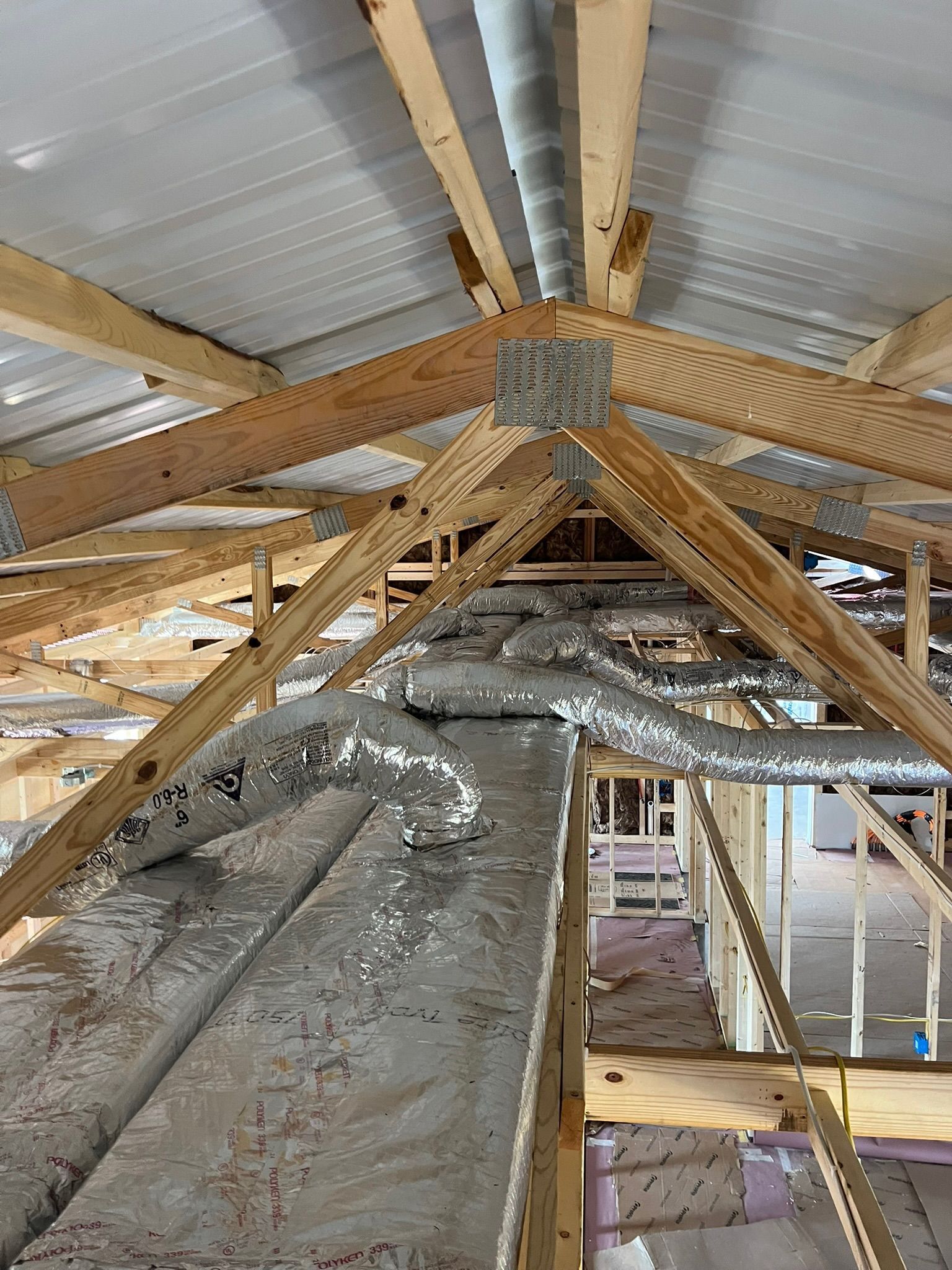Wooden roof trusses with silver ductwork and a metal roof. Construction site interior.