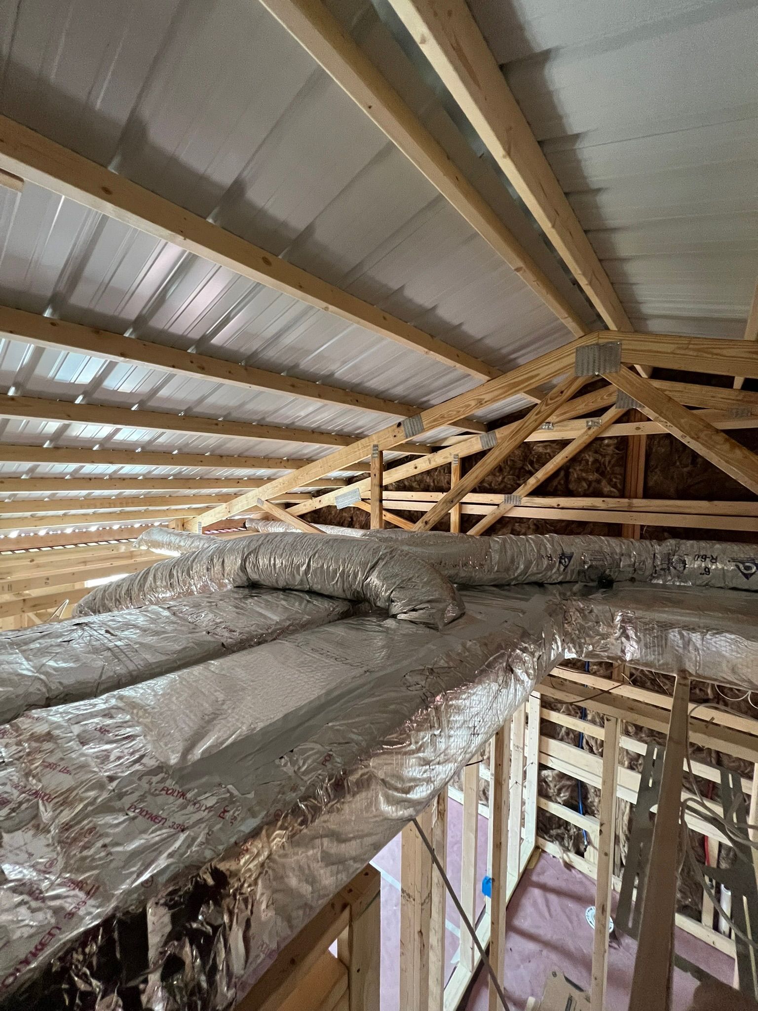 Interior view of a building under construction. Ductwork is visible, and the roof has wooden trusses.